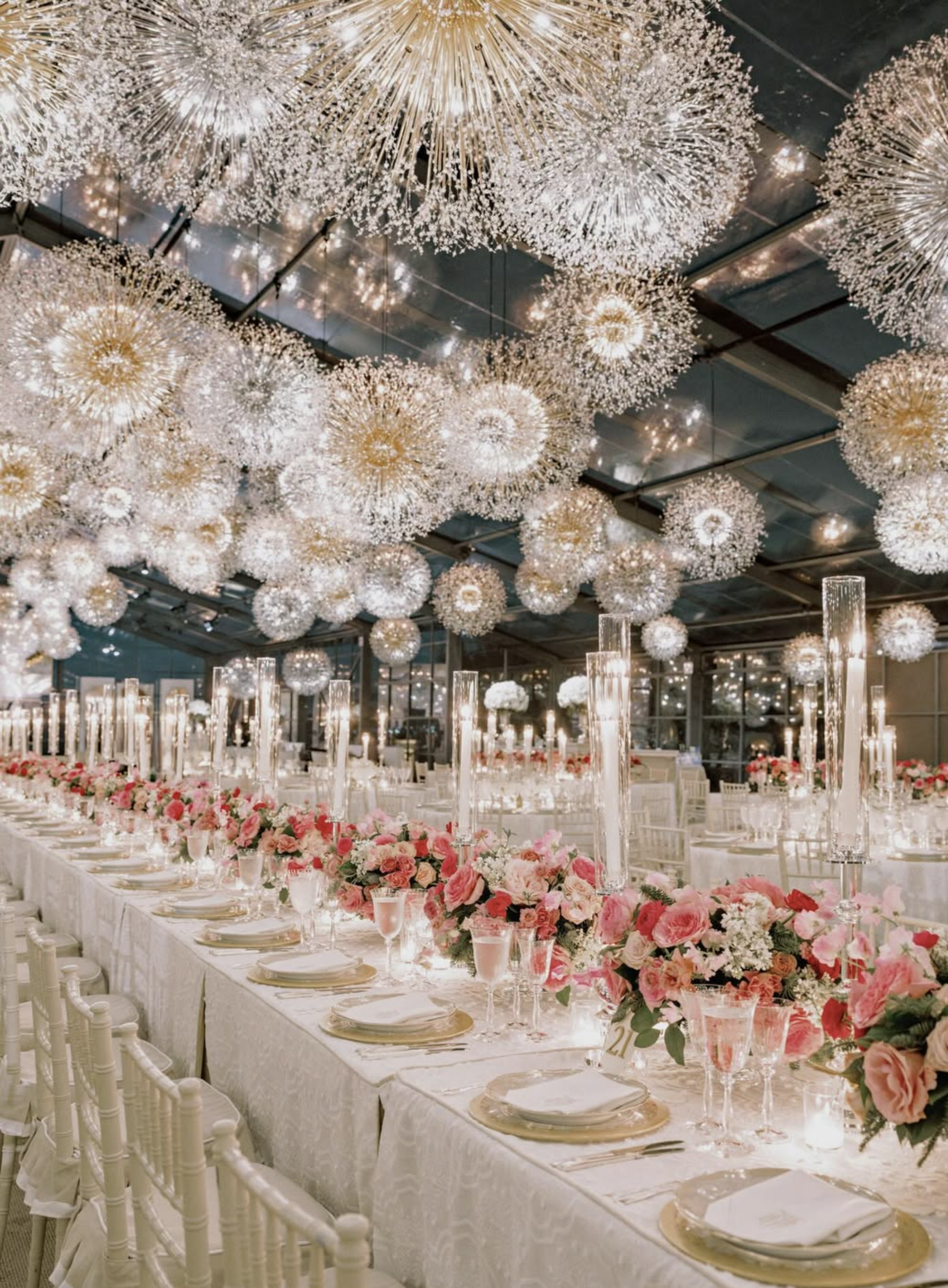 Elegant banquet hall decorated with numerous hanging spherical chandeliers, a long table set with fine china, glassware, tall candles, and a floral centerpiece with pink and white flowers.