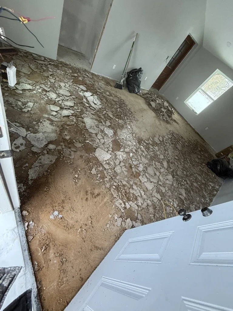 Interior of a house under renovation with a damaged, uneven floor and exposed dirt and broken flooring materials.
