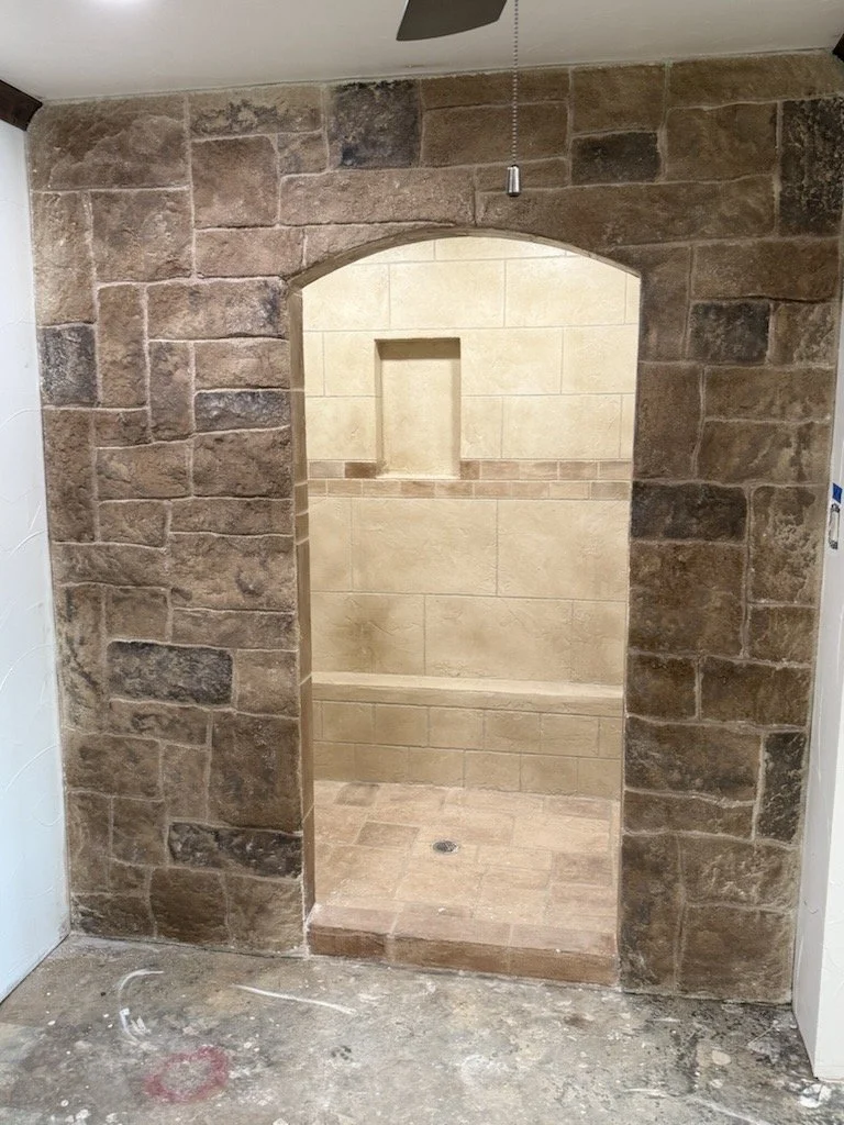 A shower with beige tiles and a built-in niche, surrounded by a wall of large brown bricks.