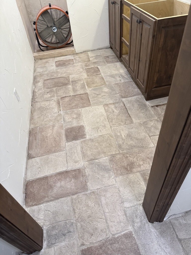 Room with beige and light brown tile flooring, wooden cabinetry, a wall-mounted fan, and textured off-white walls.