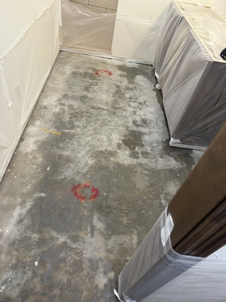 A concrete floor in a room under construction with two red spray-painted circles on the floor, covered with plastic-wrapped furniture or cabinetry along the sides.