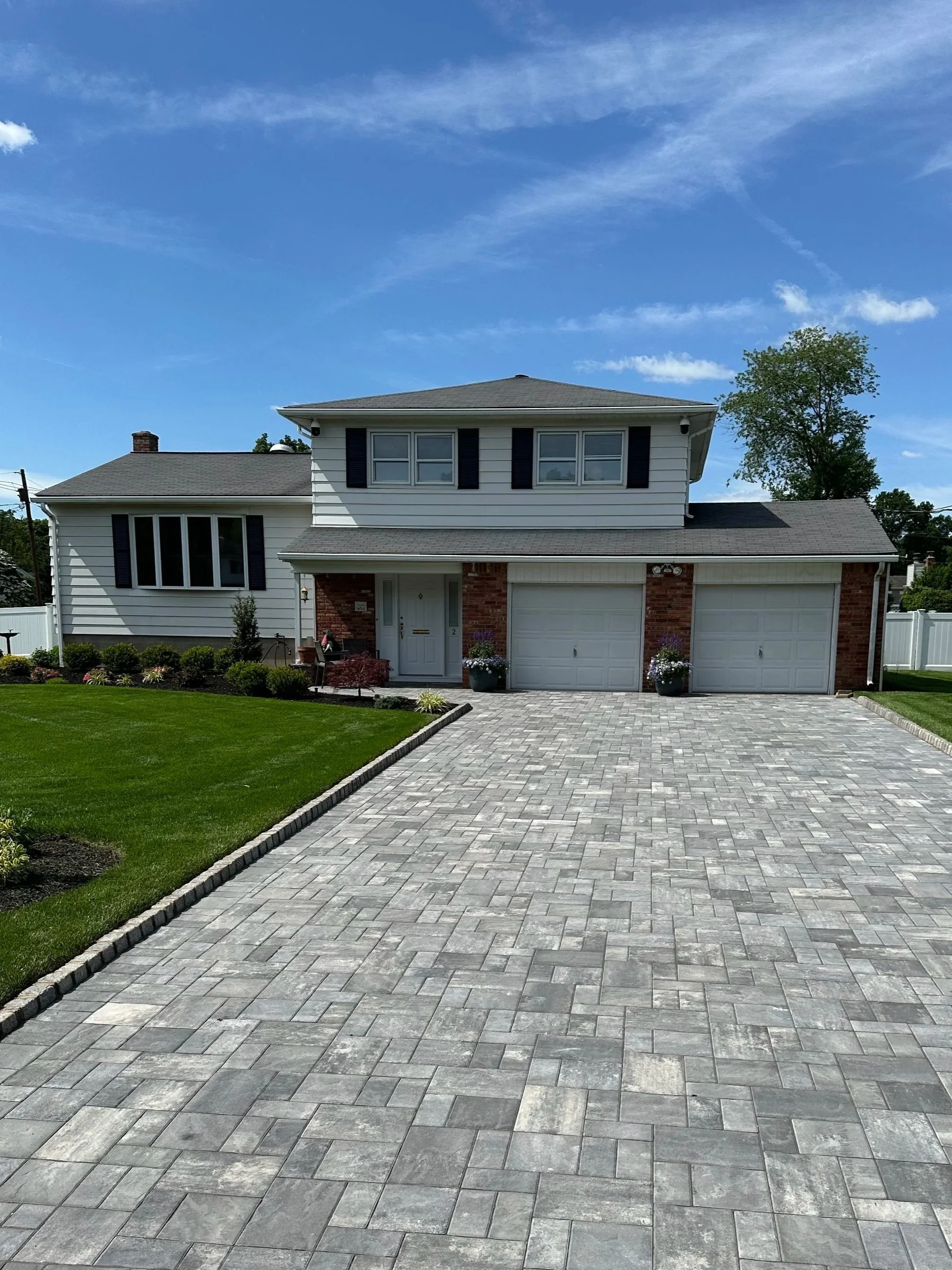 Front view of a two-story house with a driveway, landscaped yard, and a blue sky with some clouds.