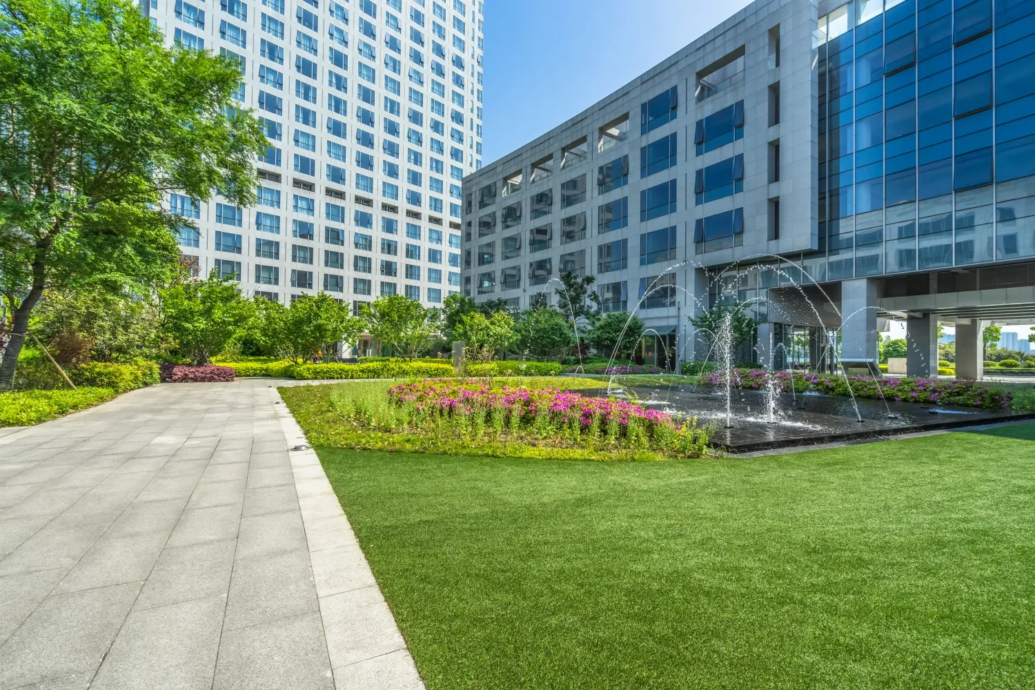 Manicured commercial lawn with colorful flower beds and a decorative fountain in front of a large office building