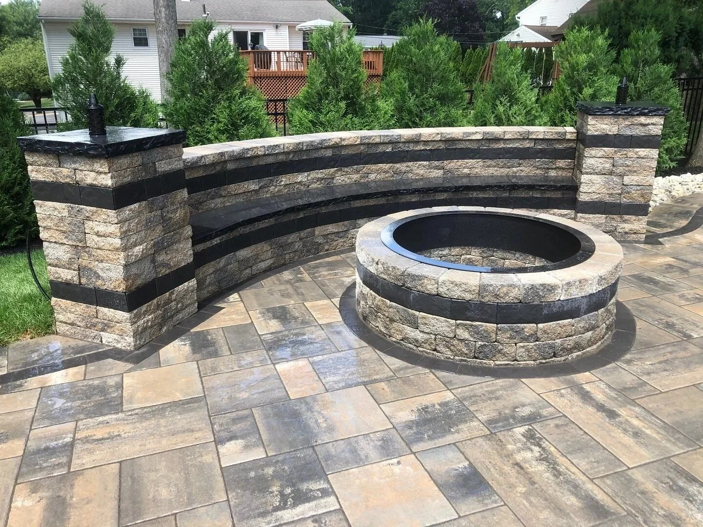 Round stone fire pit on a multi-toned paver patio with a curved seating wall — Green Nature Landscape Design