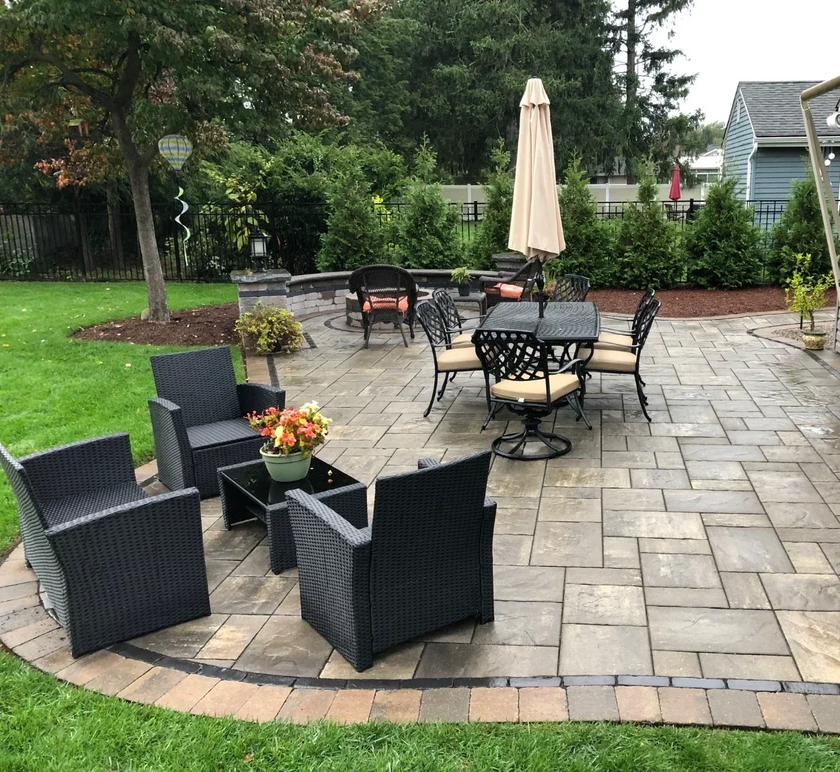 Completed paver patio with seating wall, outdoor furniture, and lush landscape plantings in a residential backyard — Green Nature Landscape Design