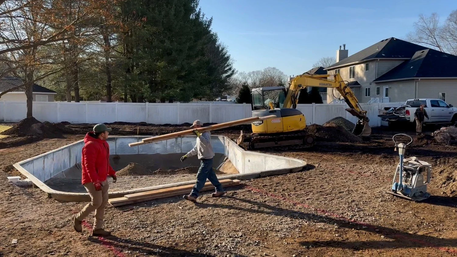 Two crew members working on a residential pool excavation site with a yellow excavator in the background. — Green Nature Landscape Design