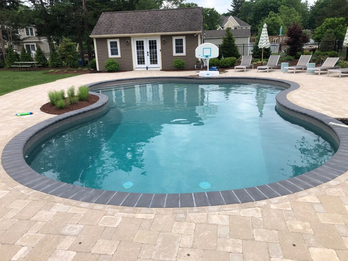 A breathtaking backyard poolscape with a freeform swimming pool and paver patio.  - Green Nature Landscape Design