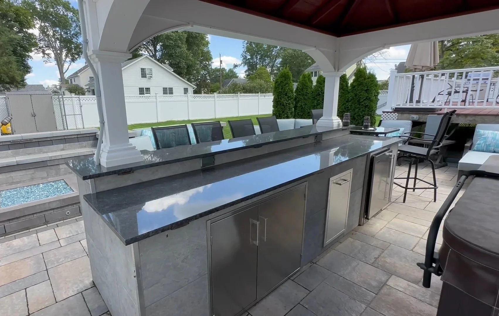 Outdoor kitchen with dark granite countertop and stainless steel cabinet doors on a covered patio — Green Nature Landscape Design