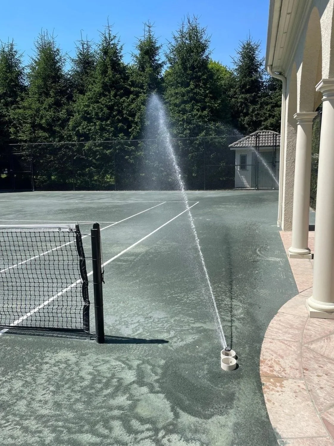 A sprinkler system watering a healthy green tennis clay court. - Green Nature Landscape Design