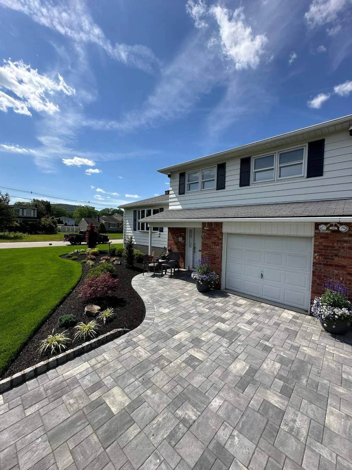Paver driveway and front entry patio with curved landscape bed, ornamental trees, and red-leafed shrubs at a two-story home. — Green Nature Landscape Design