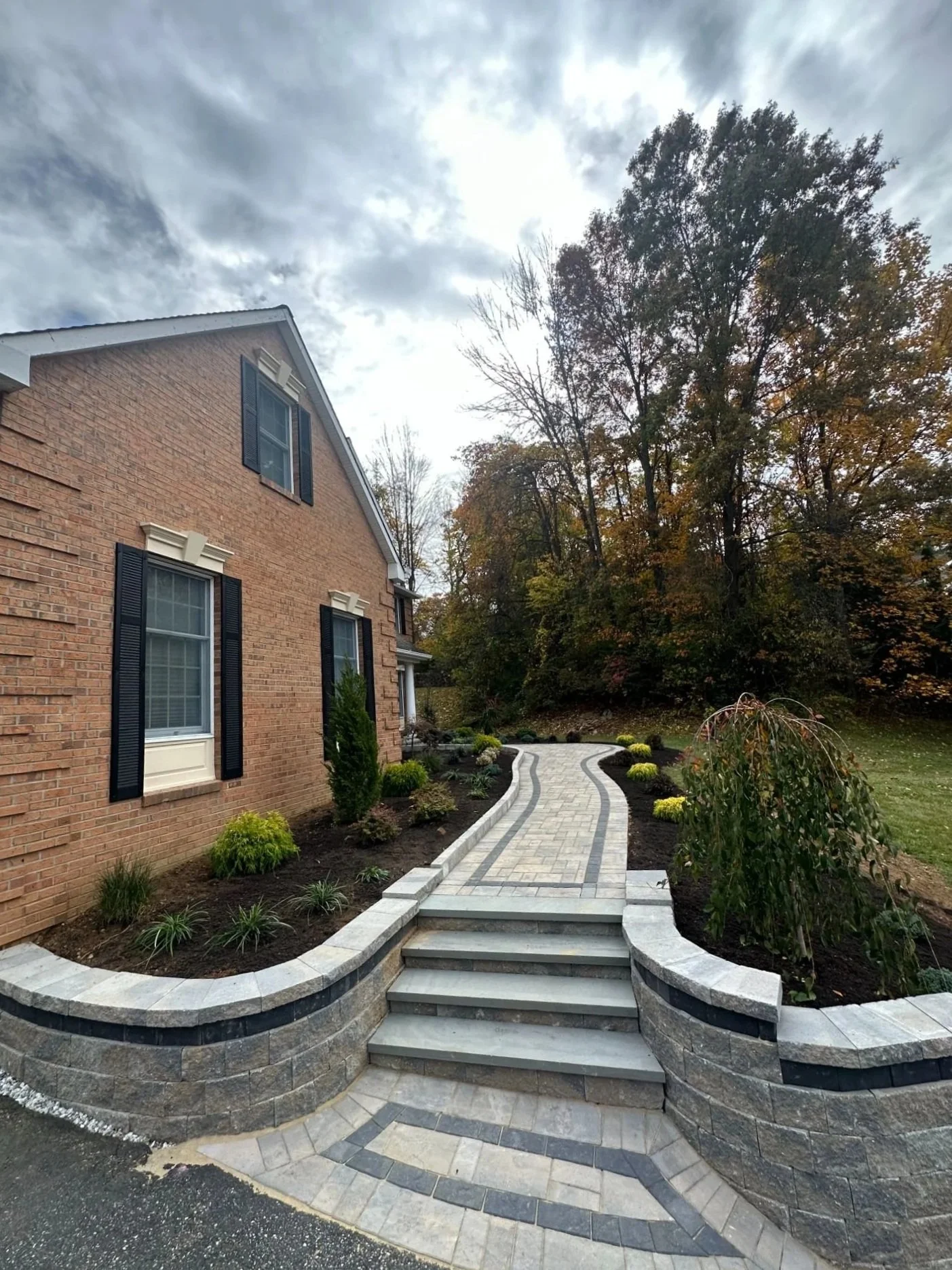 Paver retaining wall with steps and landscape plantings along the front of a brick residential home — Green Nature Landscape Design