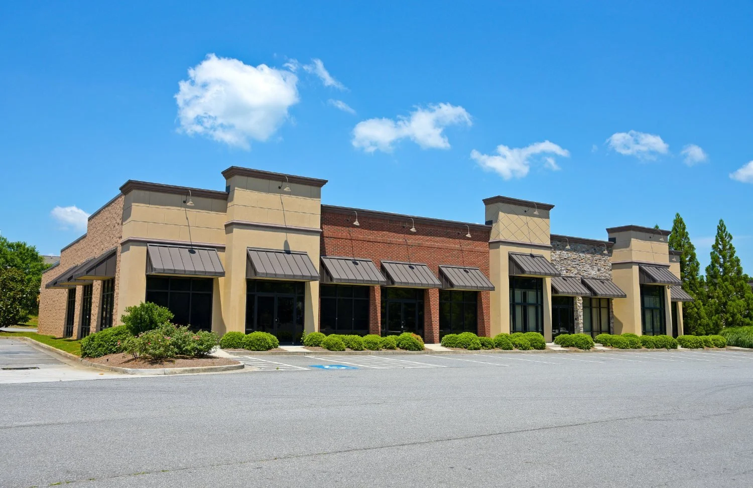 Retail shopping center exterior with low shrub landscaping along the storefront and a maintained parking area.