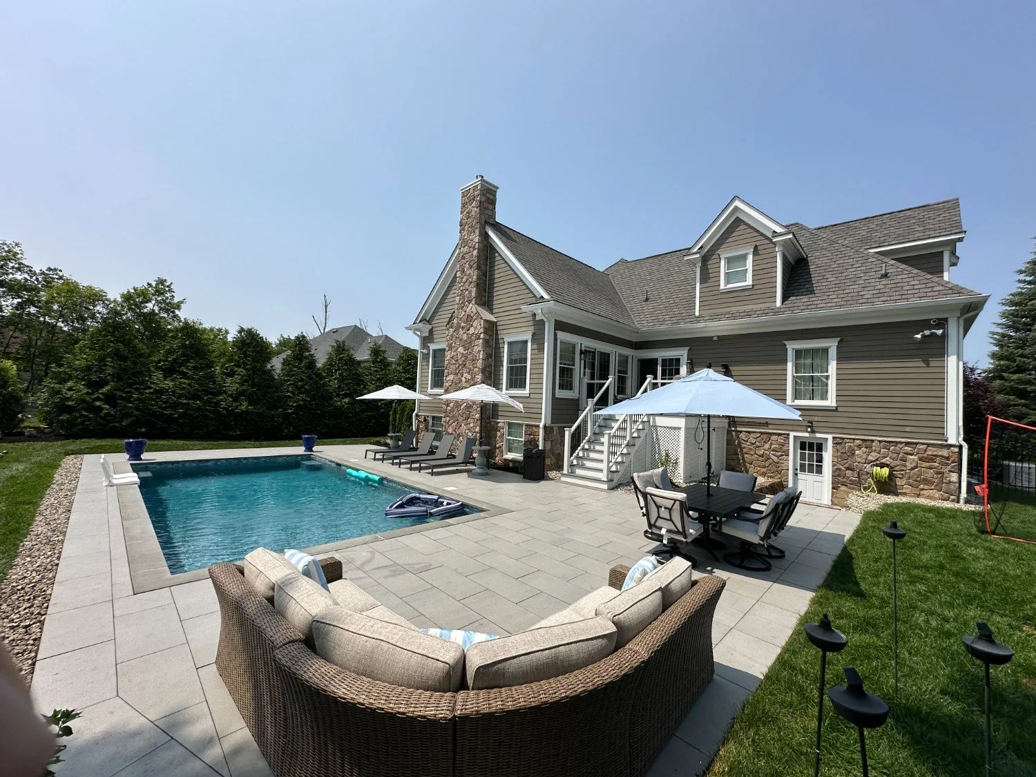 Paver patio with outdoor seating and dining area alongside a residential pool and stone home — Green Nature Landscape Design