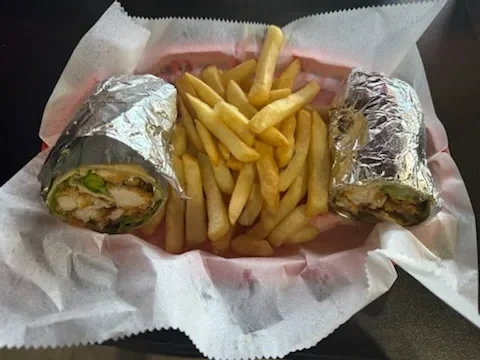 Two foil-wrapped burritos with French fries on pink wax paper
