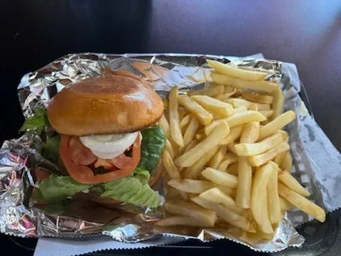 Hamburger with lettuce, tomato, and onion, served with French fries on foil-lined tray.