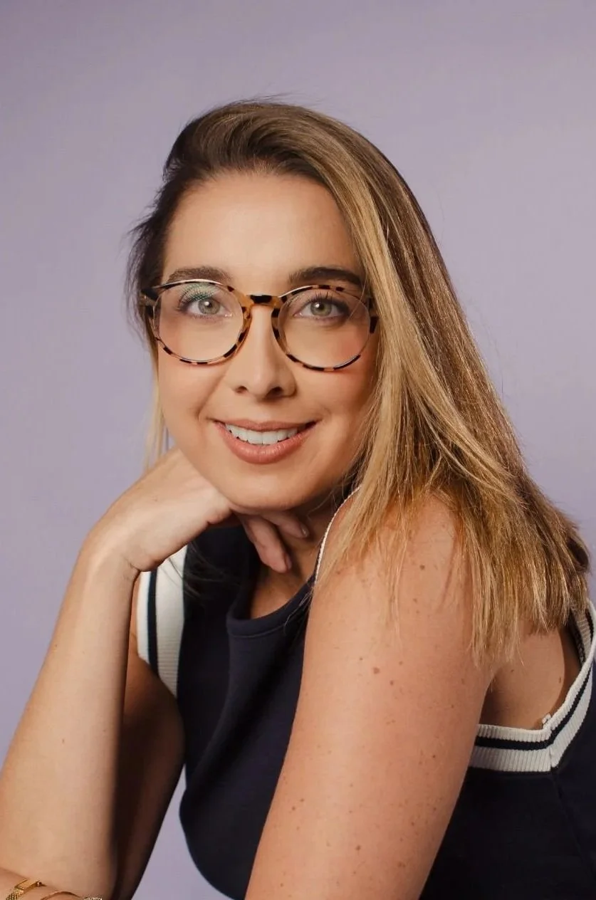 Smiling woman with shoulder-length brown hair wearing a navy blue top against gray background.