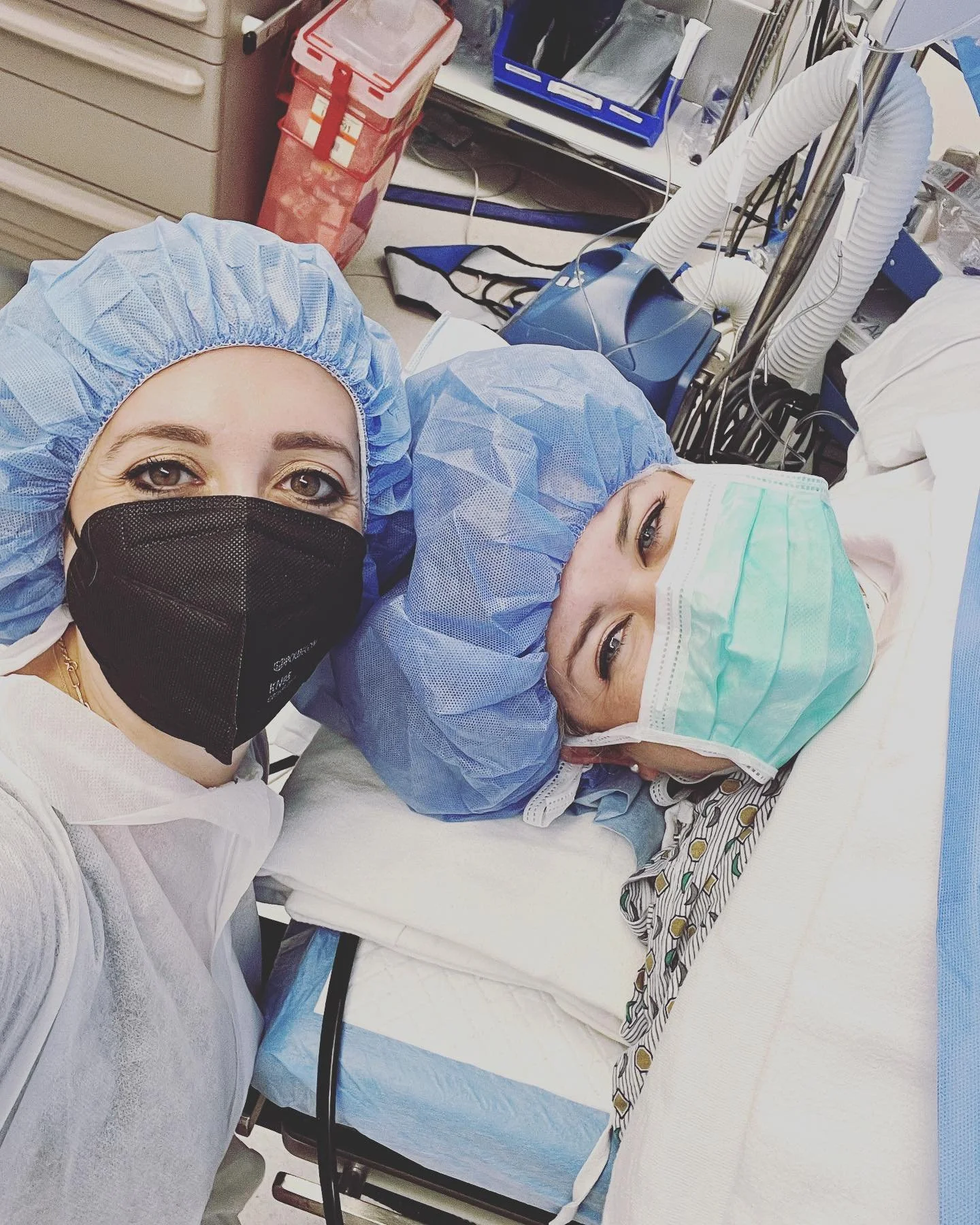 Hospital staff wearing masks and protective gear taking a selfie with a patient lying in a hospital bed.