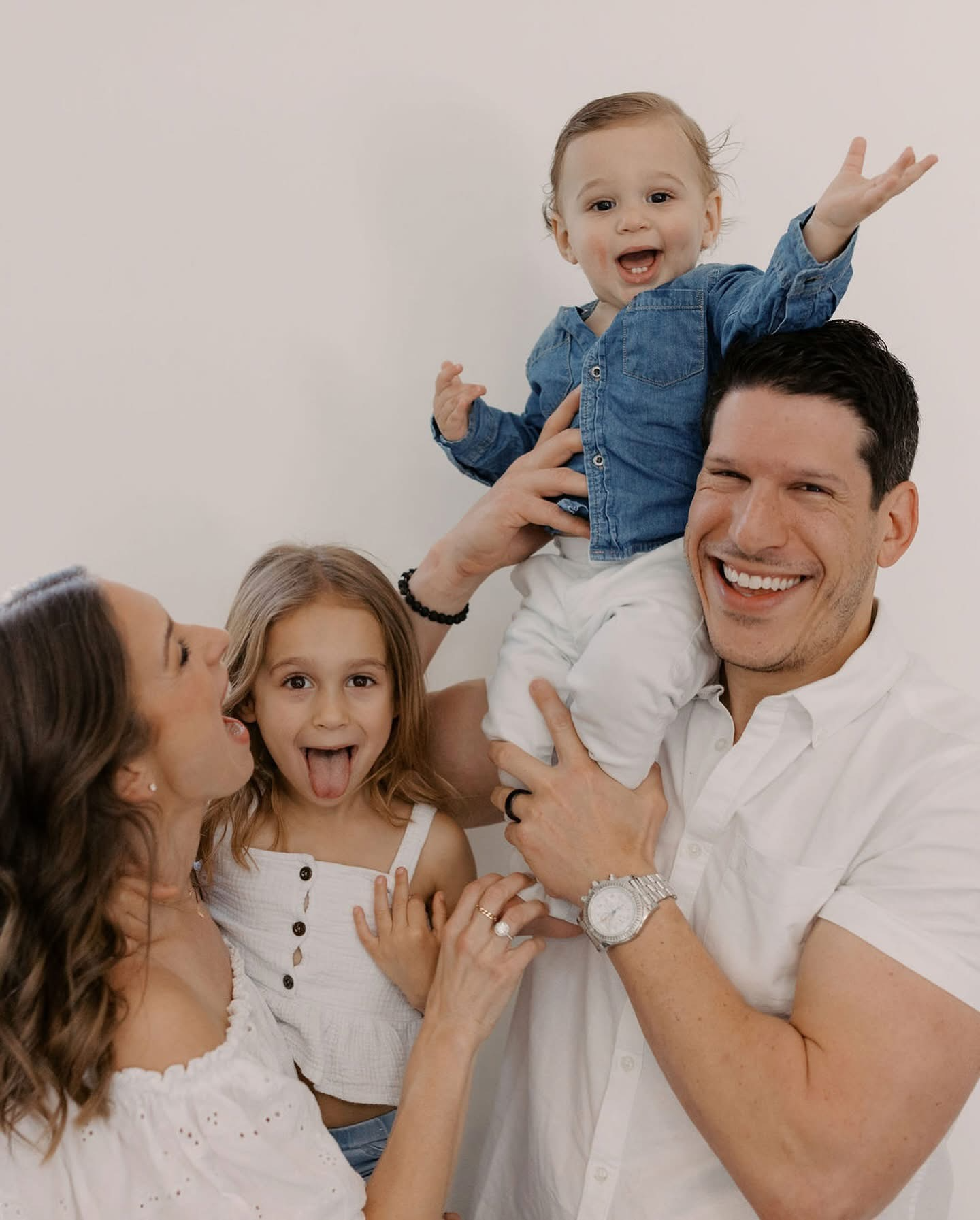 A happy family of four together, with a child sitting on their father's shoulder, all smiling.