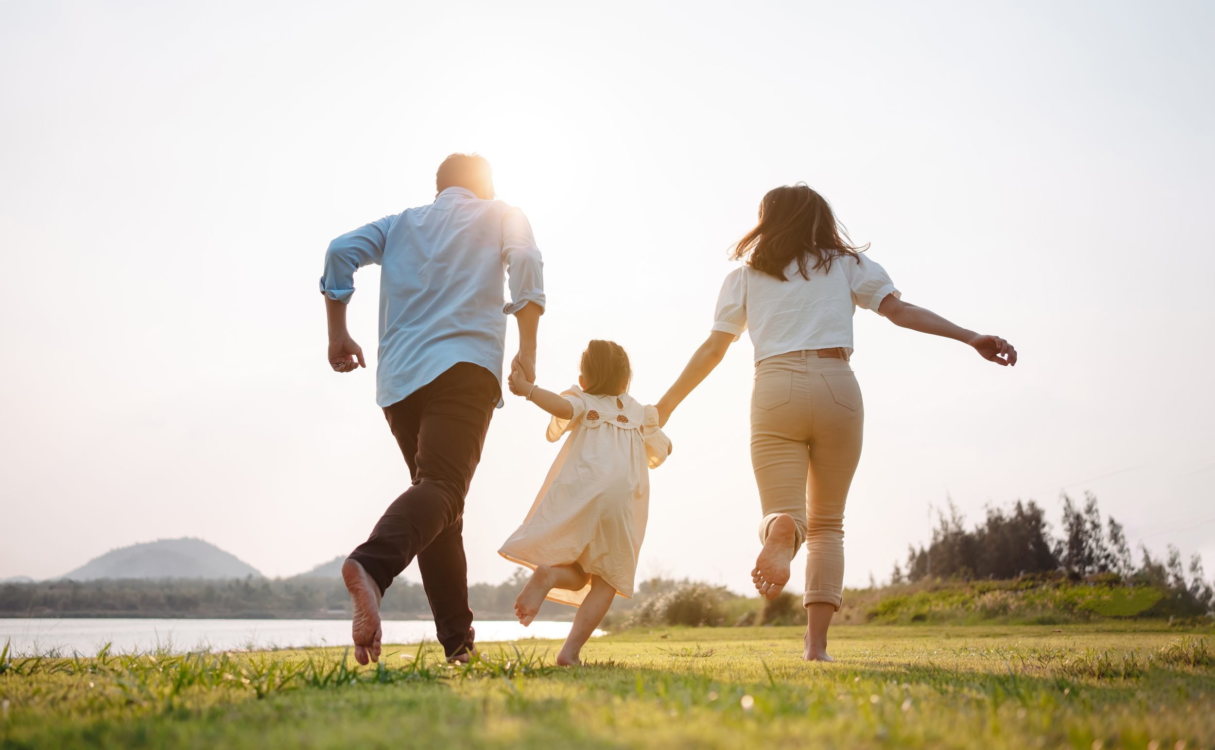 Two parents holding their young child's hands as they run together
