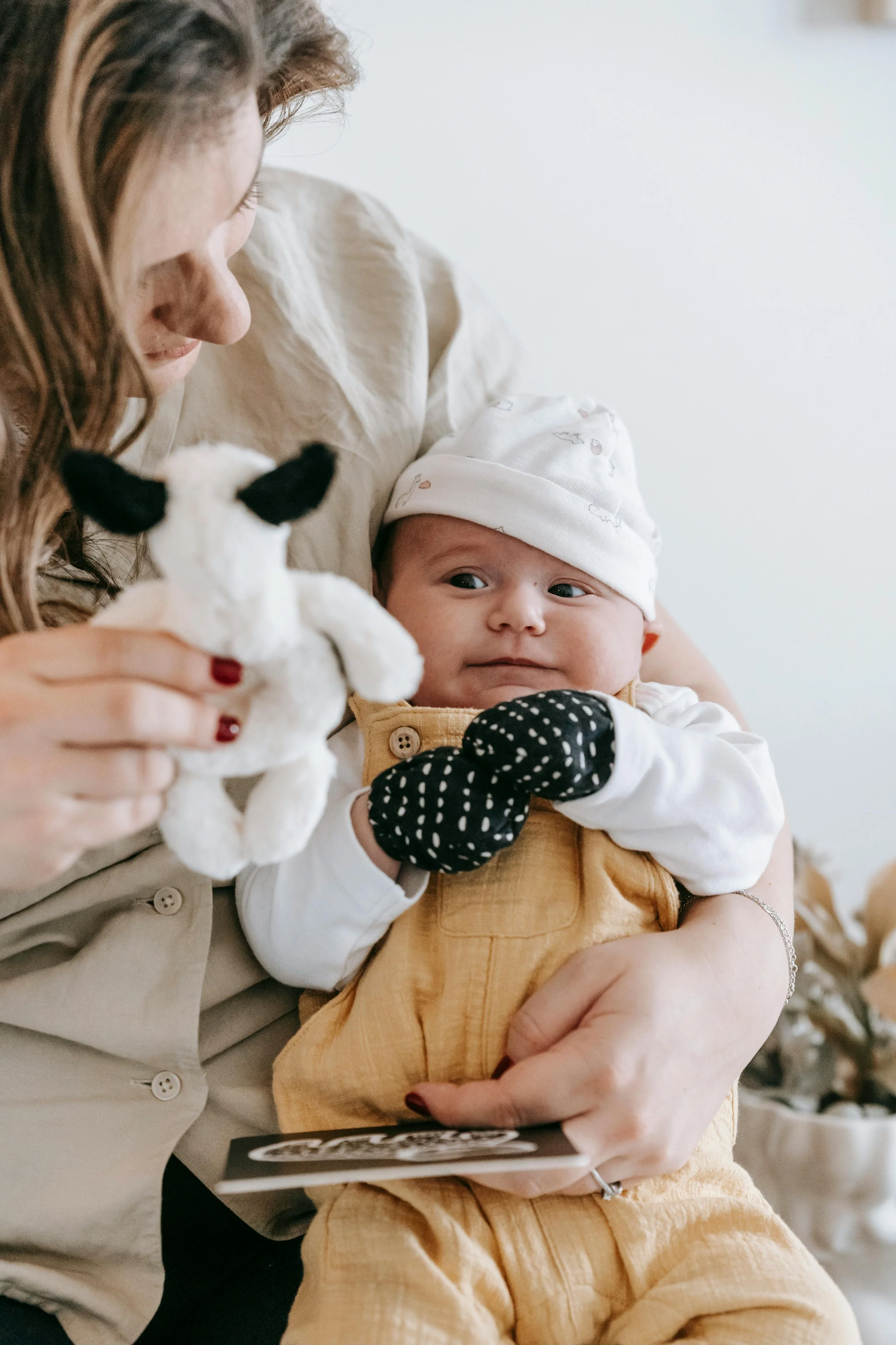 A woman holding a baby who is playing with a small stuffed cow toy.
