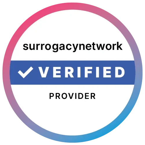 A circular badge with a pink and purple gradient border, white background, and a blue band across the middle. The text reads 'surrogacy network VERIFIED PROVIDER'.