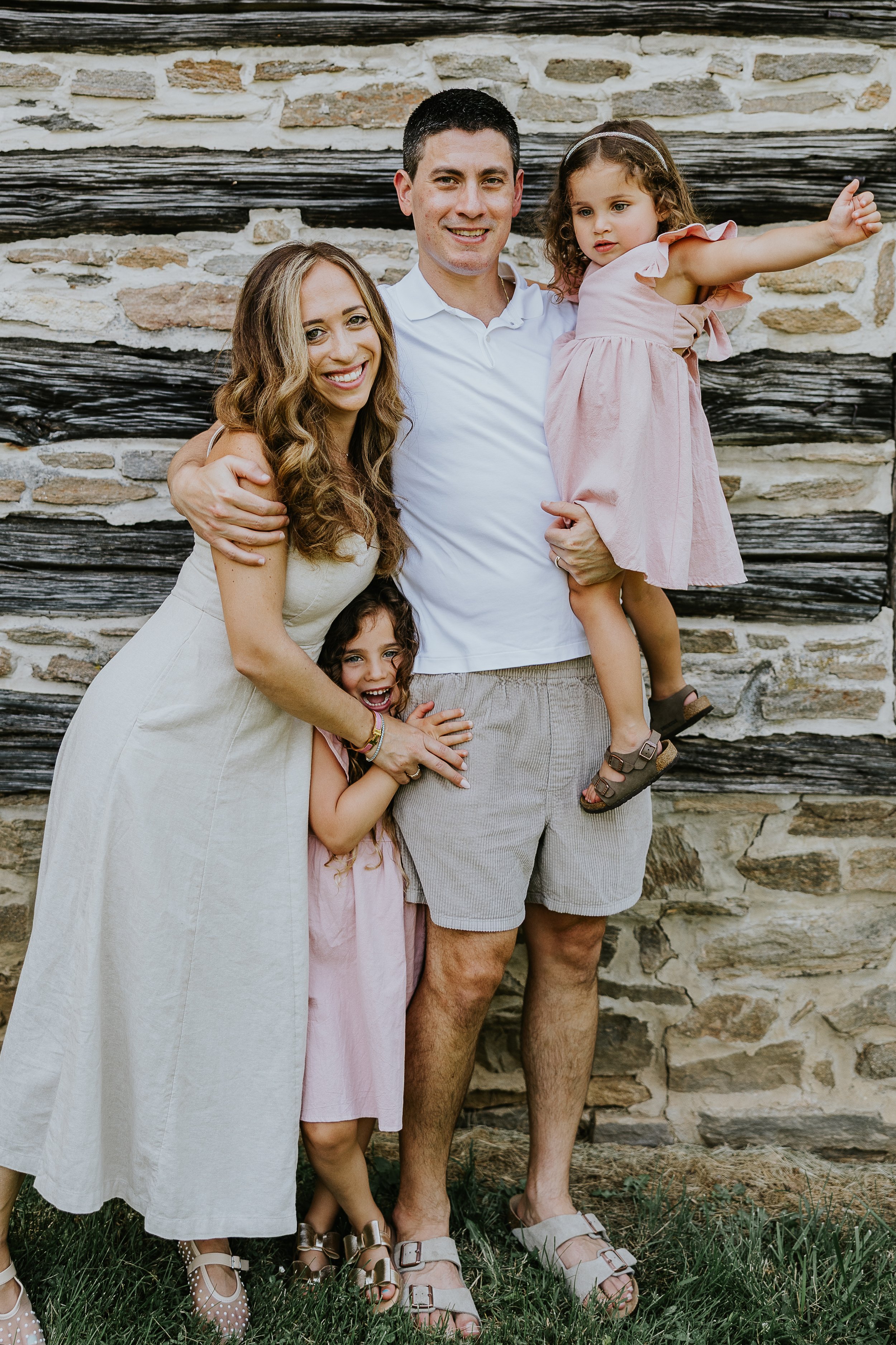 A family of four standing in front of a stone and wood wall, smiling and posing for a photo.