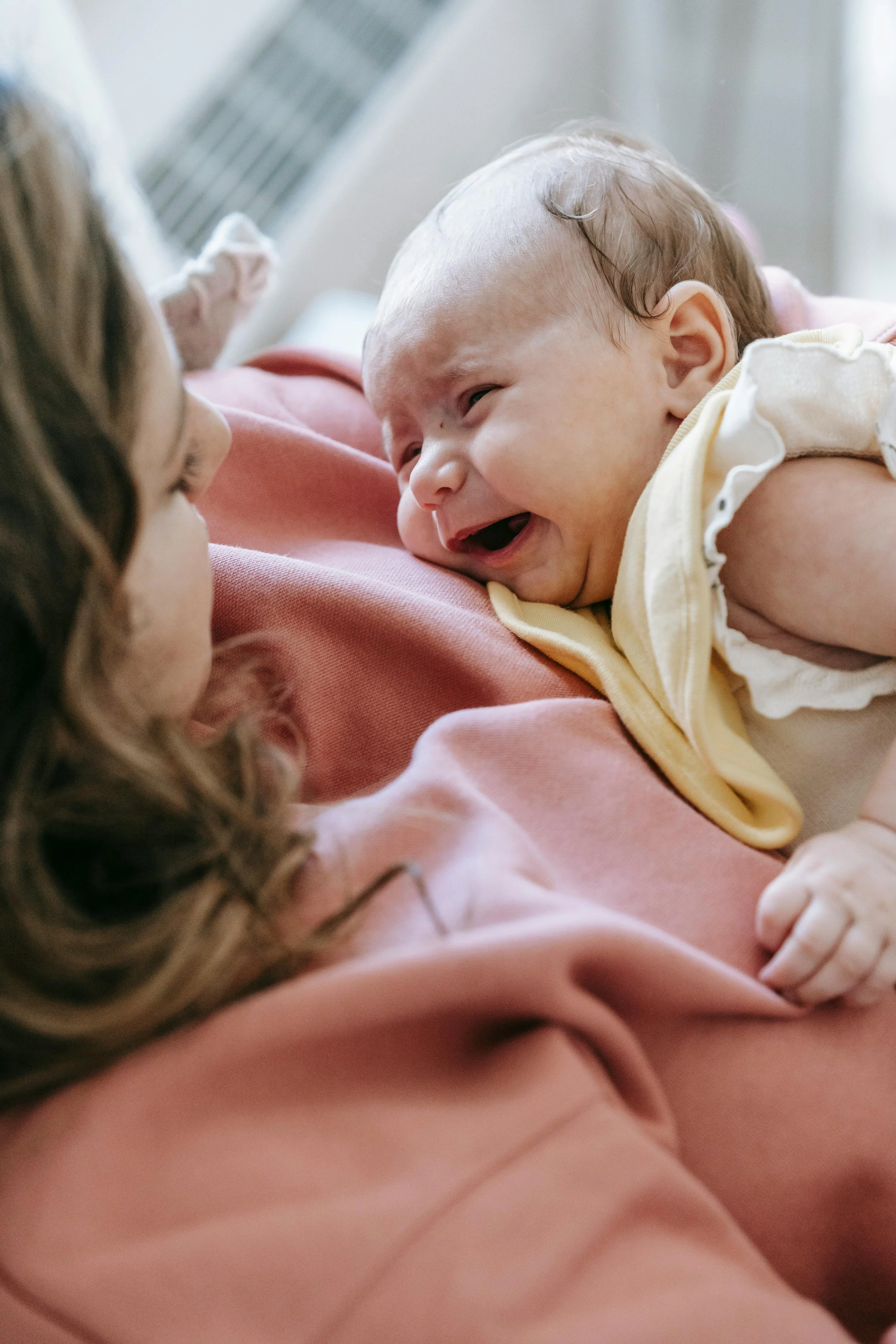 A baby lying on an adult's chest, smiling and looking at the adult, who is holding the baby gently.