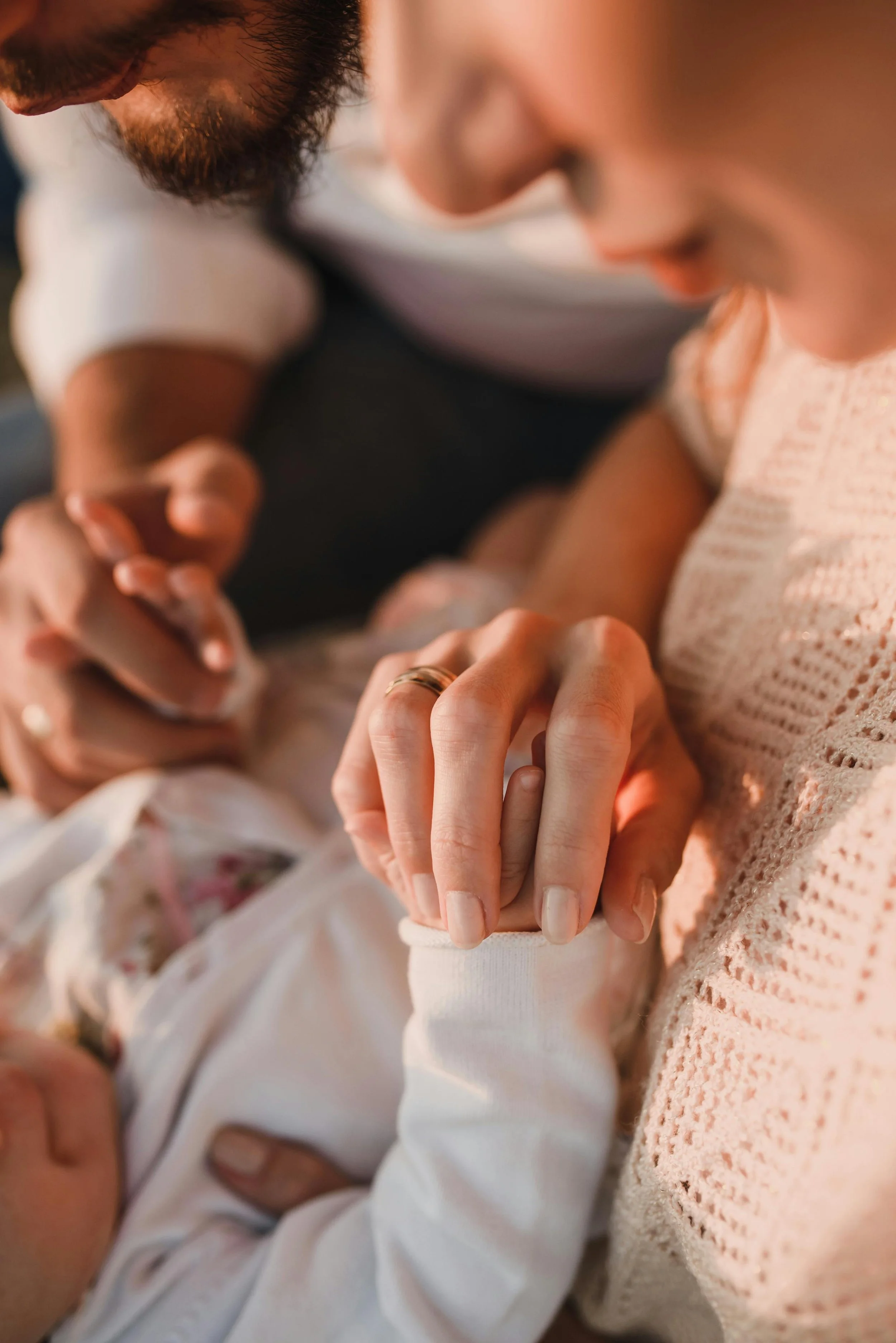 Close-up of a man and woman holding hands, with the woman wearing a white sweater and a wedding ring, and the man with a beard, both leaning closely together.