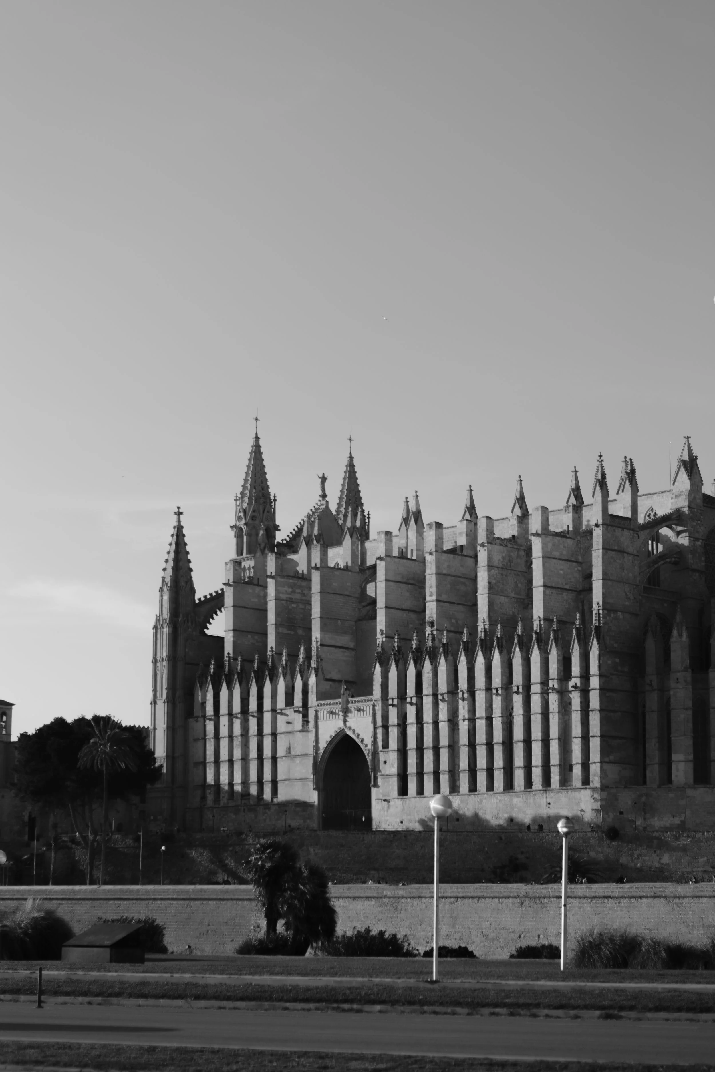 A black and white photograph of a gothic style cathedral with pointed spires and detailed architecture, captured in an outdoor setting with trees and a grassy area in the foreground.