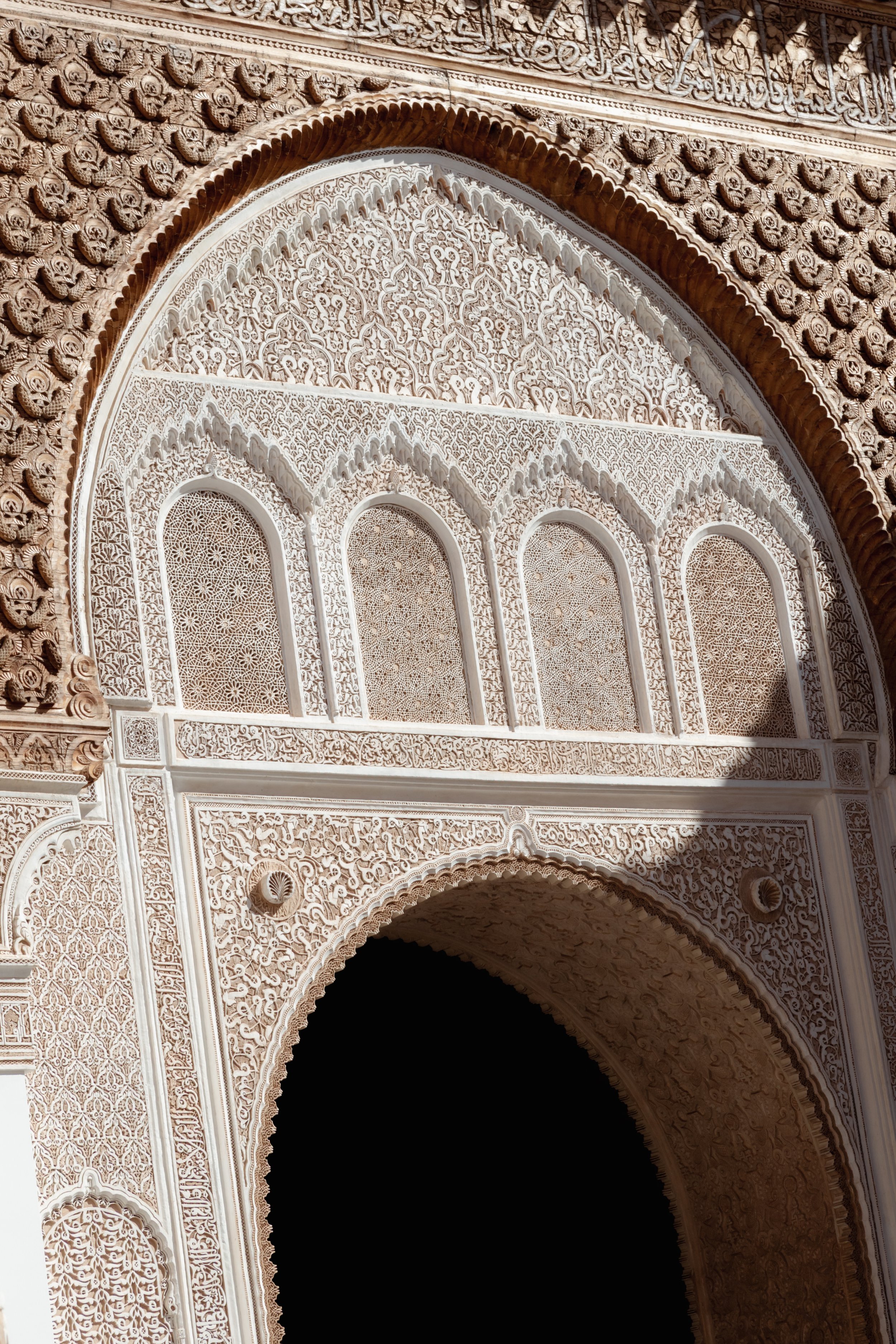 Intricate white marble archway with detailed Islamic geometric and floral patterns, casting shadows on ornate carvings and a dark interior.