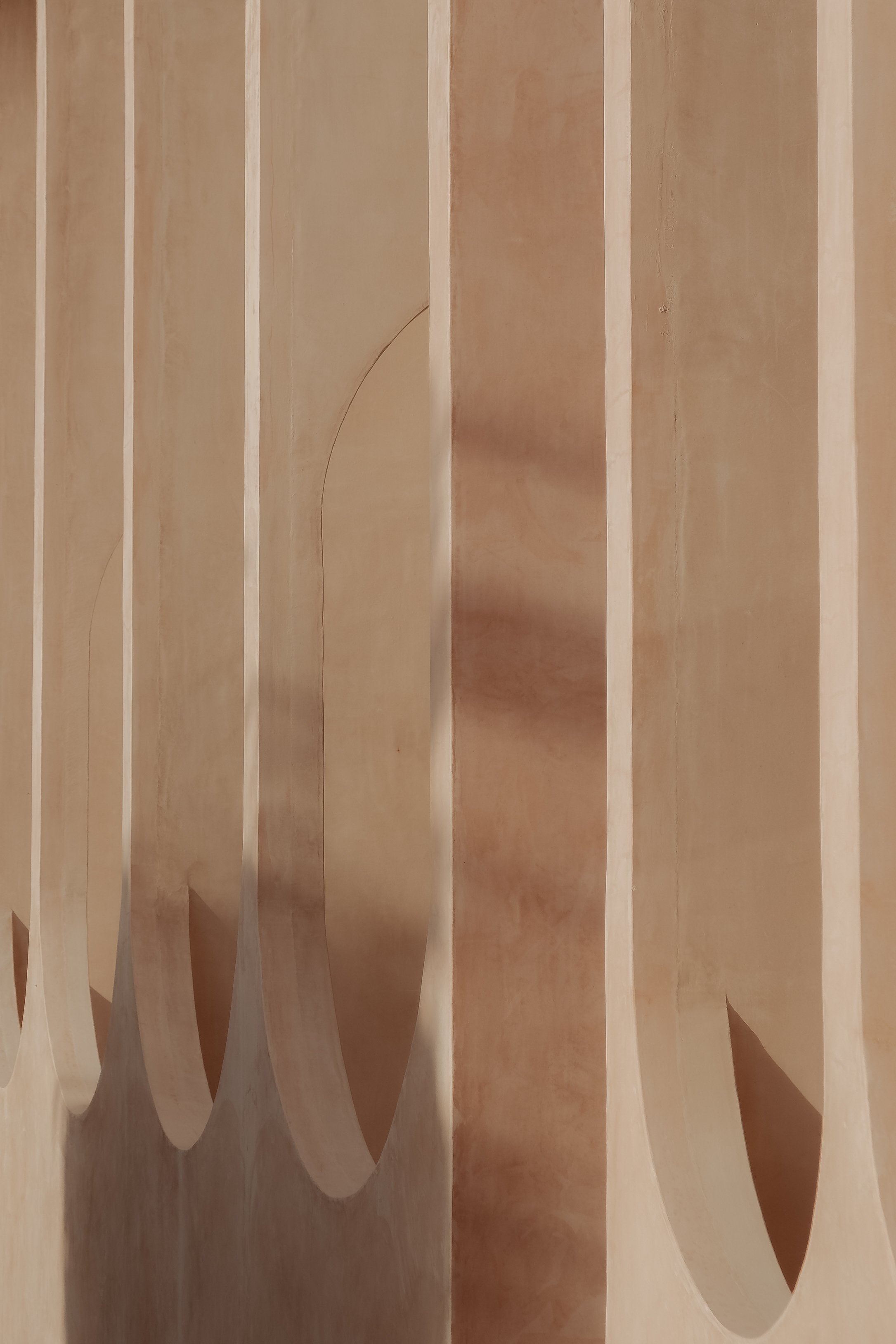 Close-up view of wooden vertical slats or panels with curved edges, creating a pattern of alternating light and shadow.