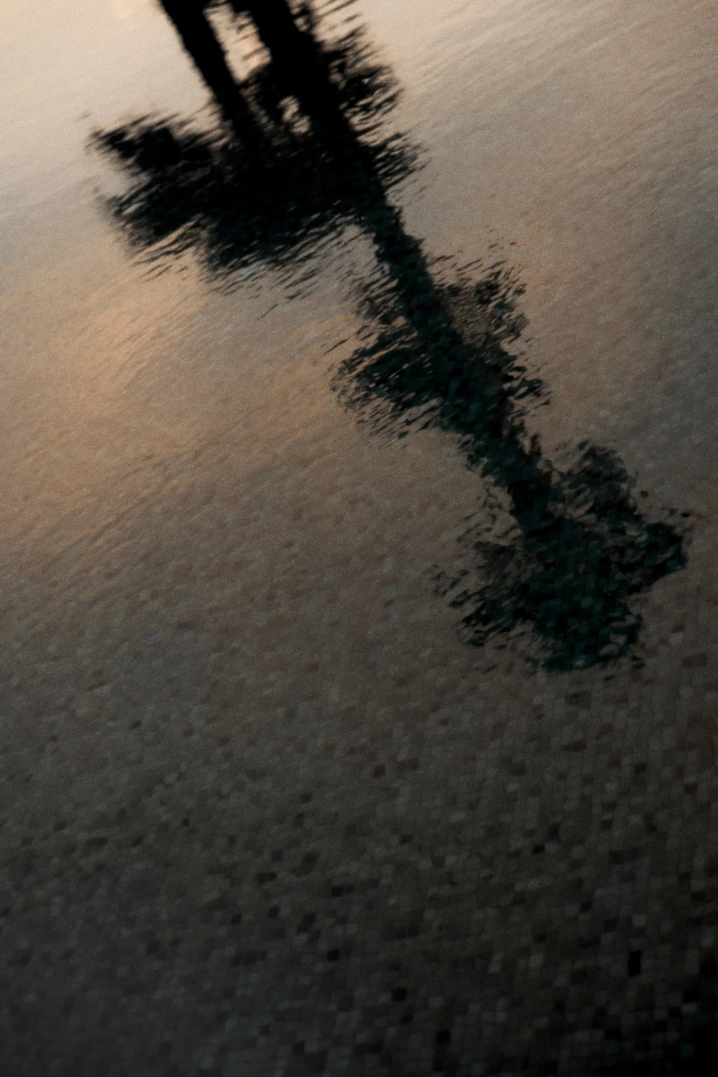 A shadow of a cross on a textured wall, possibly a ceiling or floor, with a gradient of brownish-grey and beige tones.