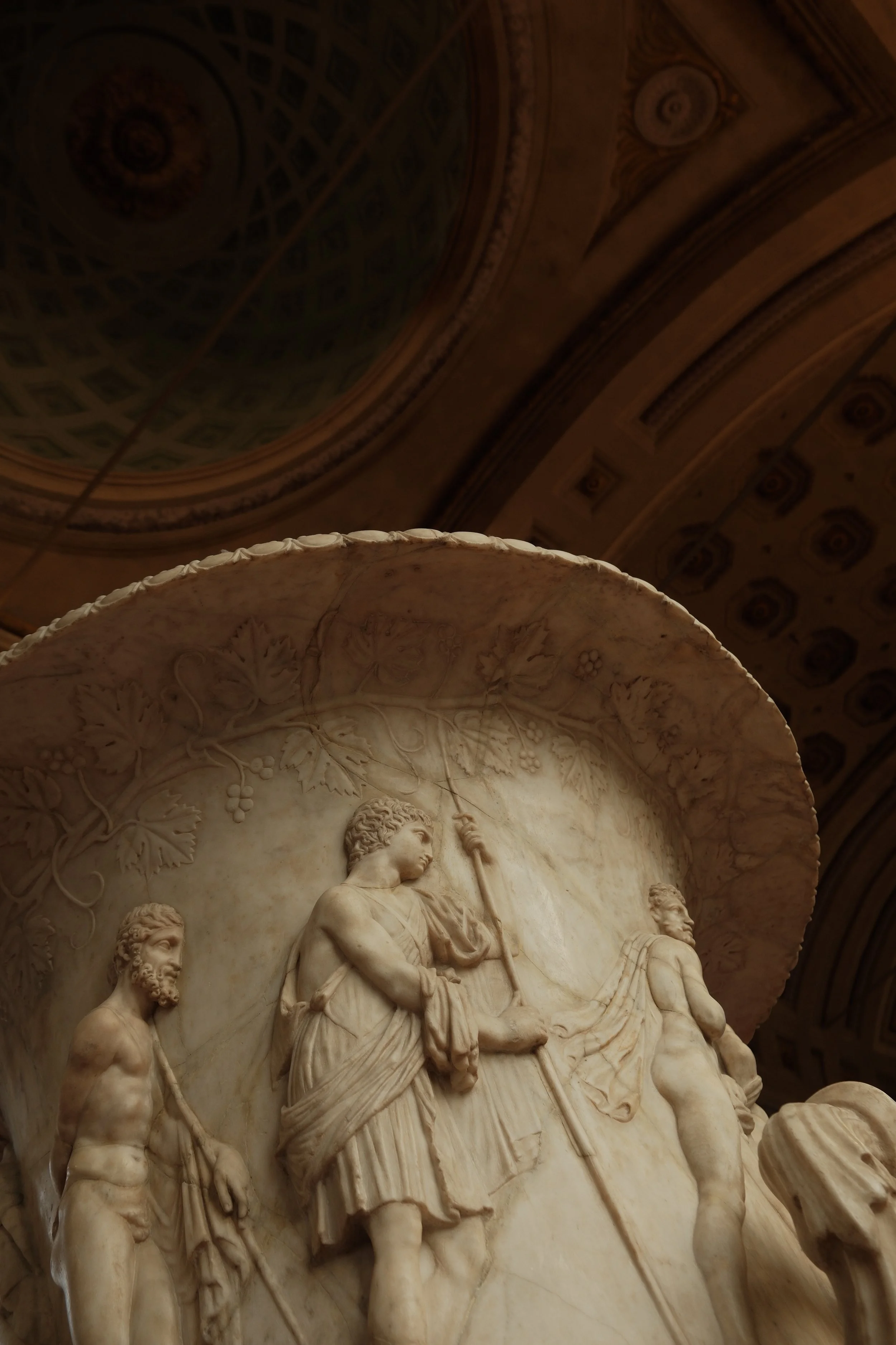 Close-up of a detailed marble relief sculpture depicting historical or mythological figures with a decorated arch ceiling in the background.