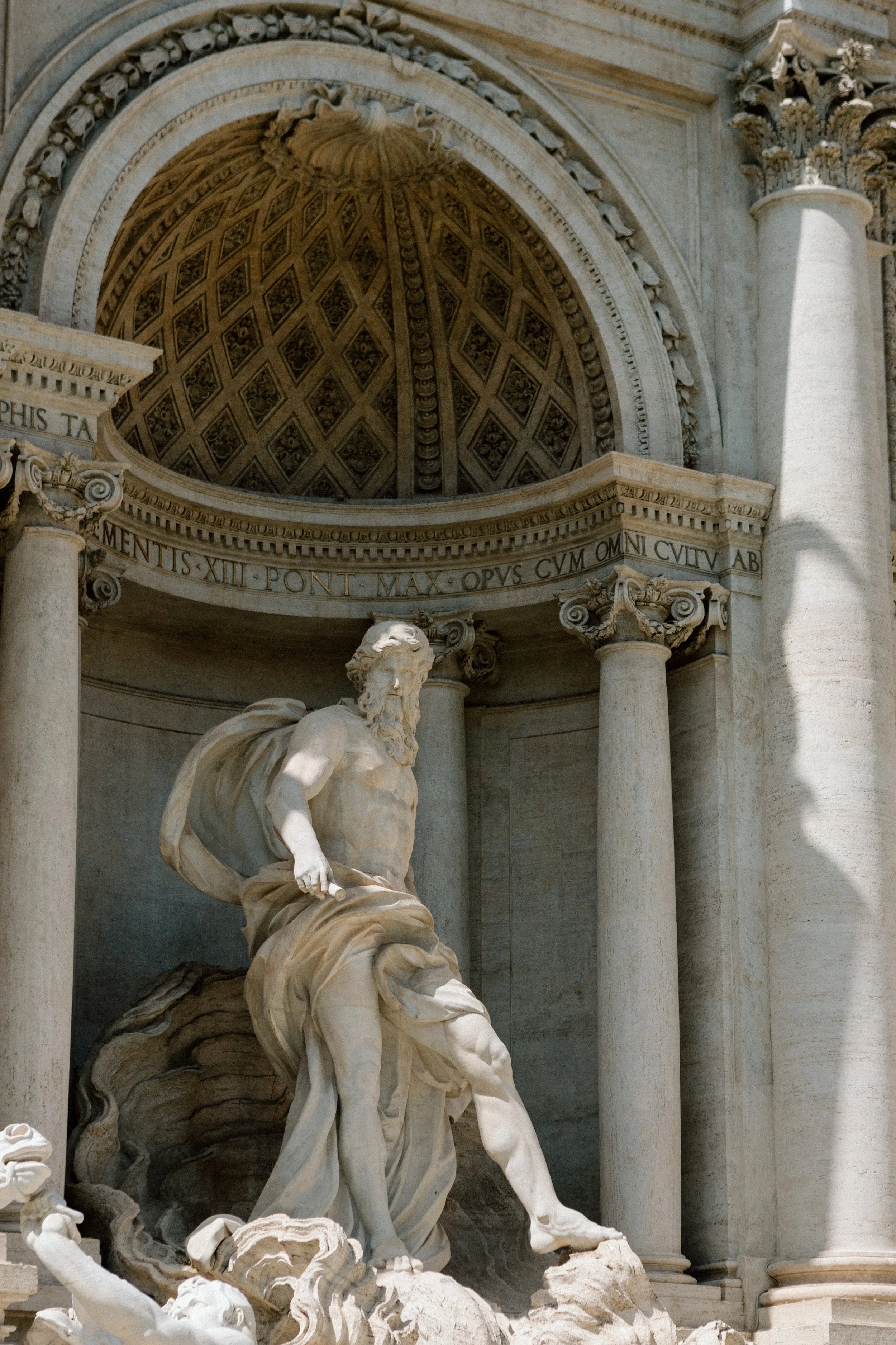 A marble sculpture of a muscular man in a dynamic pose, with a partially damaged base, set against an ornate architectural background with columns and an arch with detailed carvings.