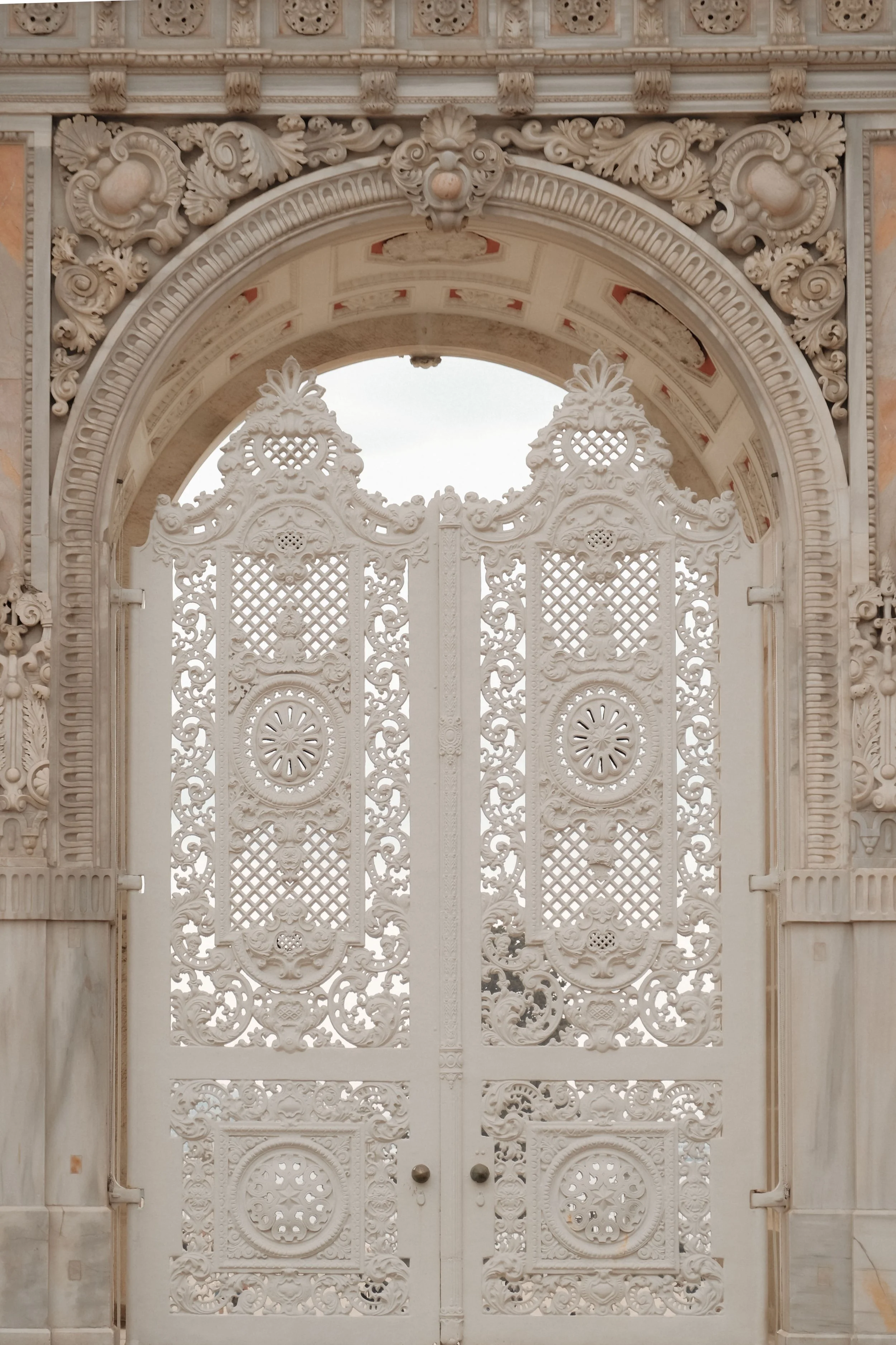 Ornate white carved gate with intricate floral and geometric patterns, set within a marble frame.