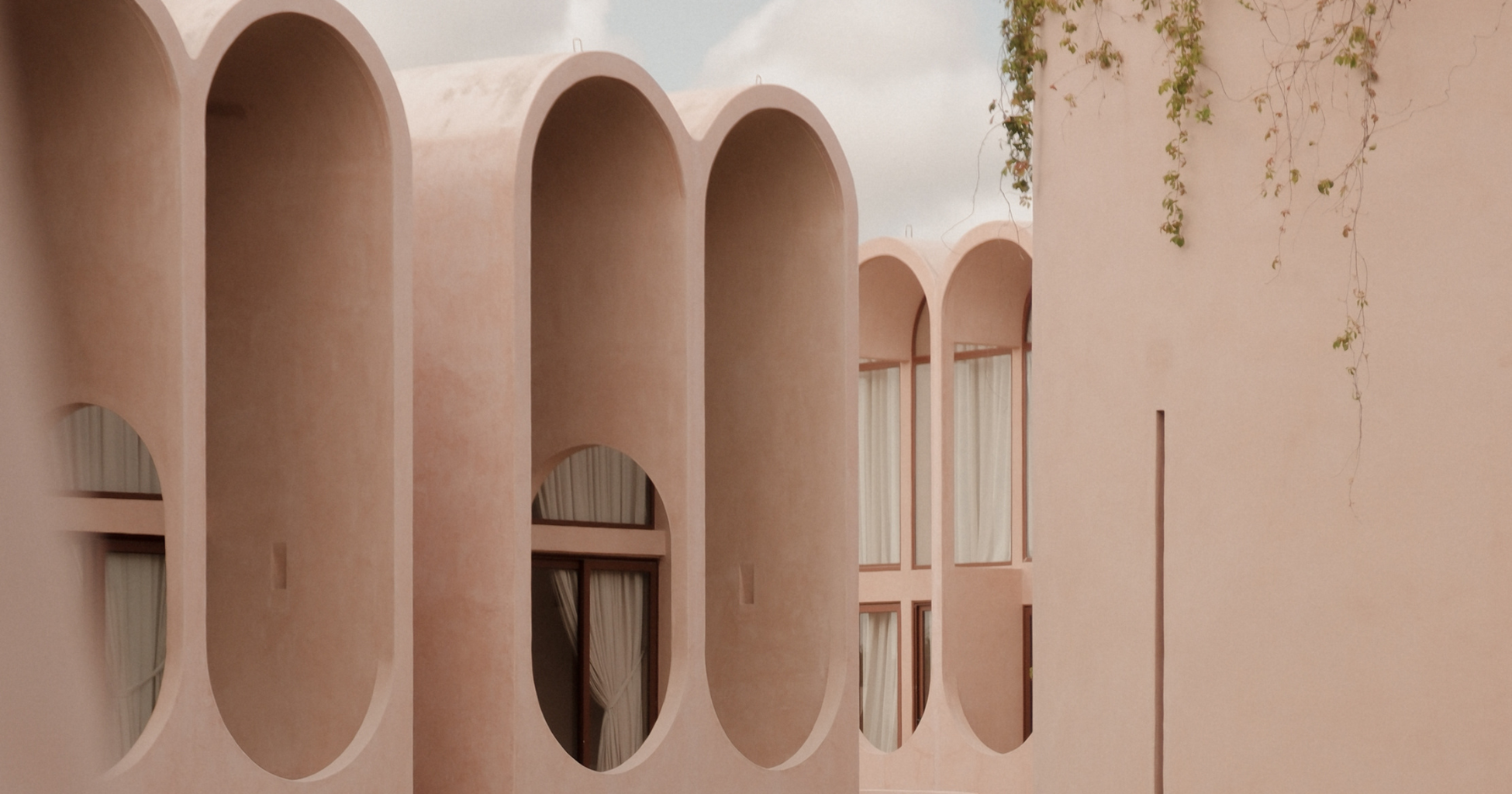 A building with peach-colored walls and rounded arch windows, with some greenery and vines on the exterior.