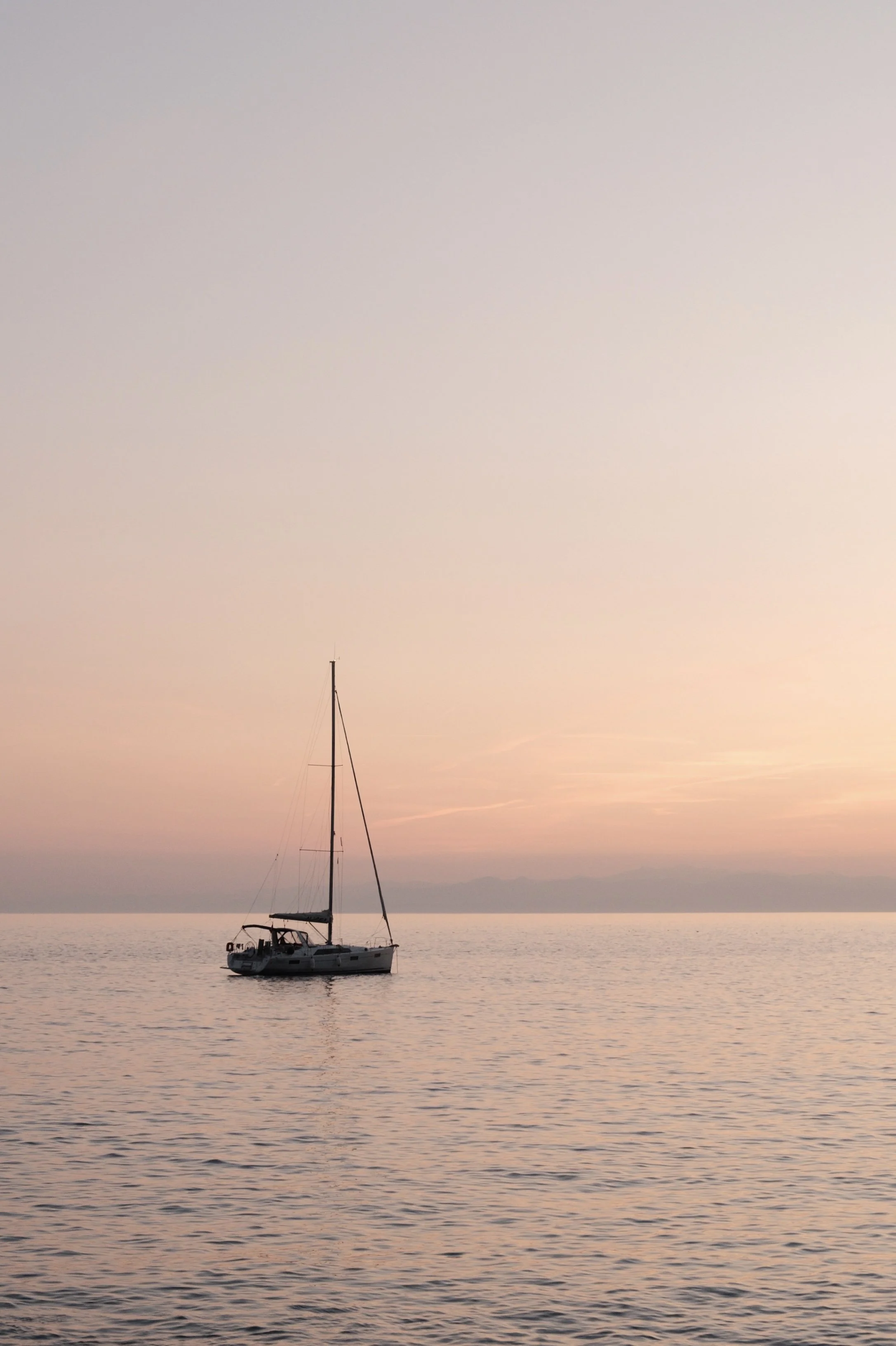Sailboat on calm water at sunset or sunrise with soft pastel sky.