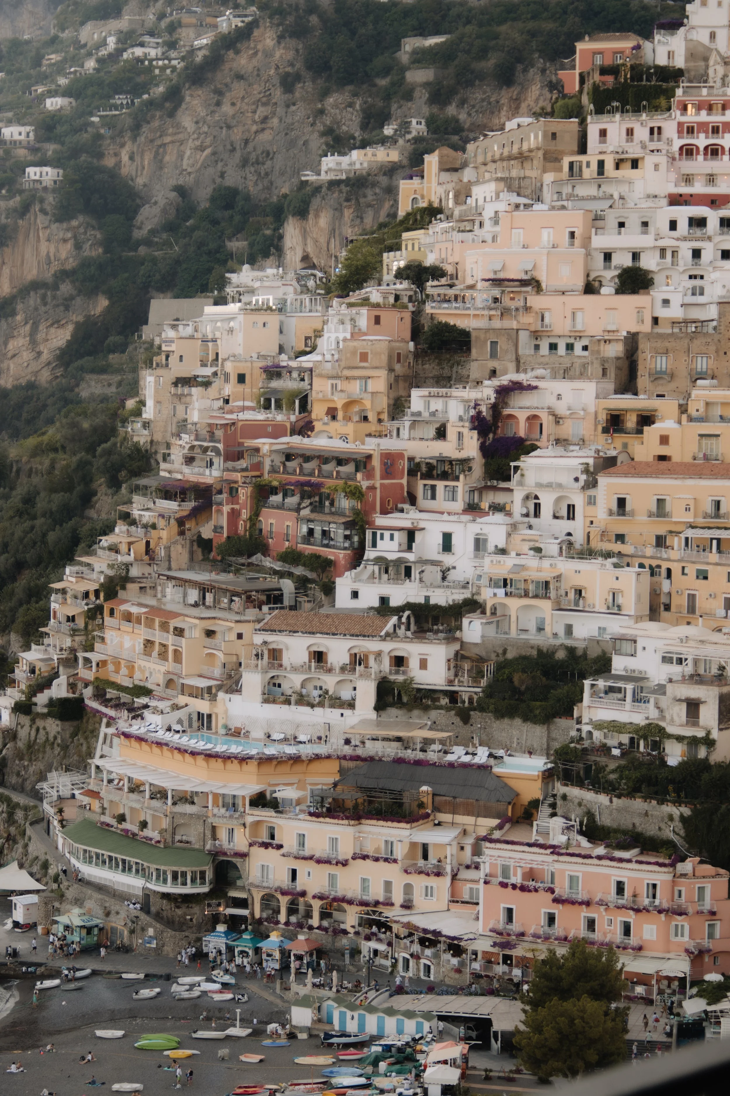 Colorful houses built on a hillside above a beach with boats and people, overlooking the sea.