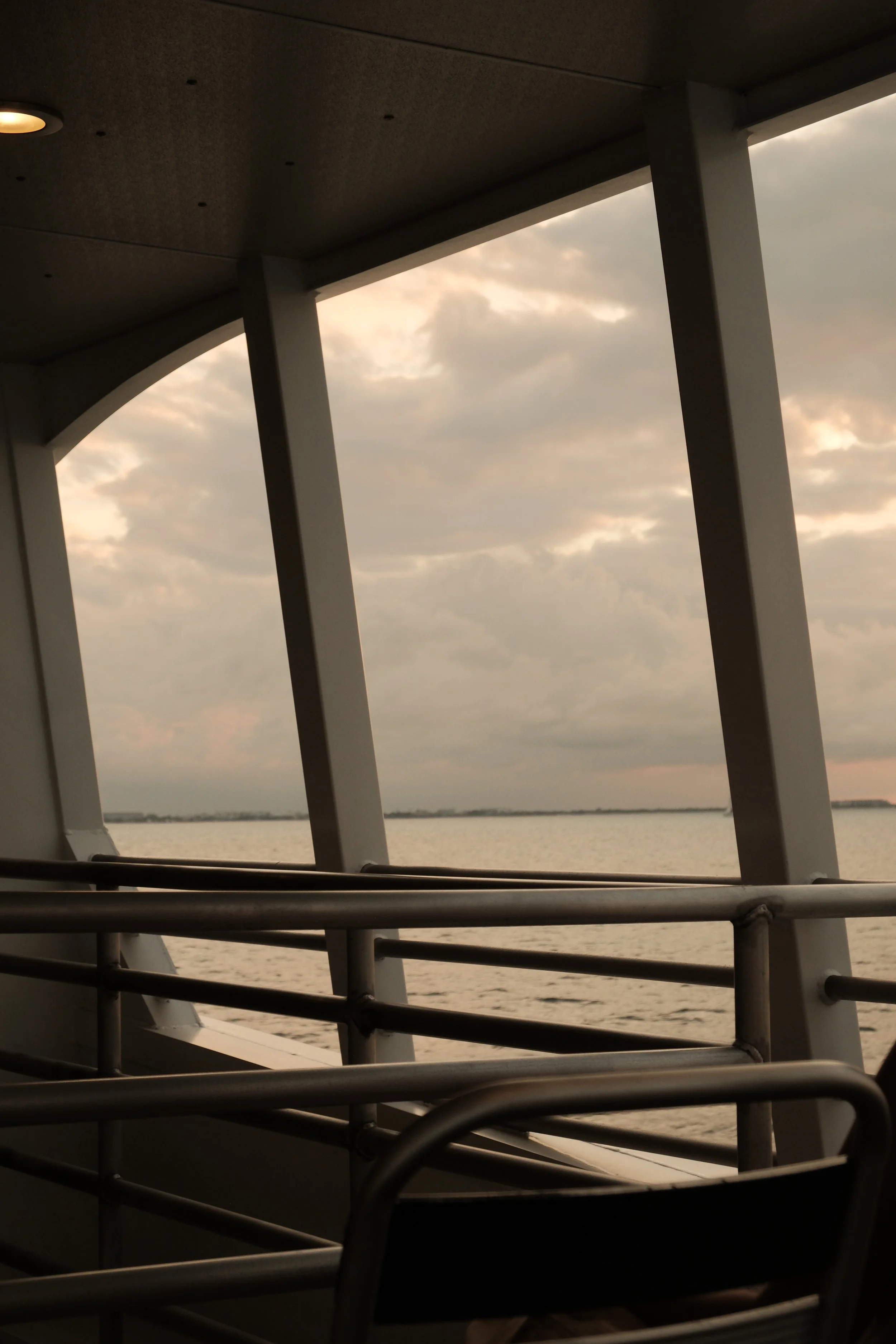 View of an overcast sky and water seen through the structural beams of a bridge or balcony, with railing in the foreground.