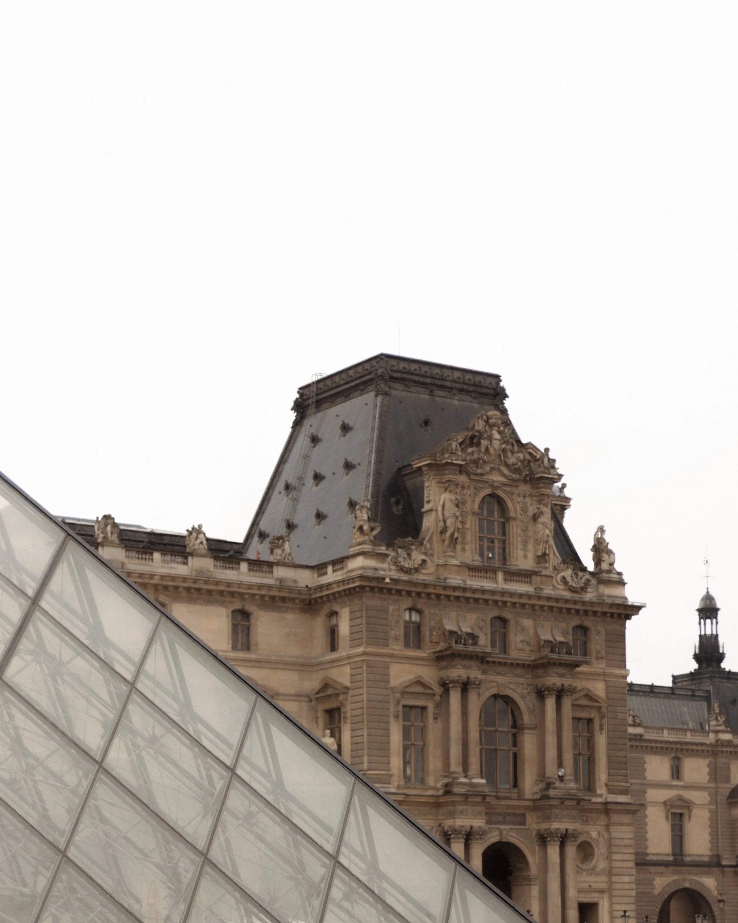 A historic building with ornate architecture and sculptures, partially obscured by a modern glass structure in the foreground.