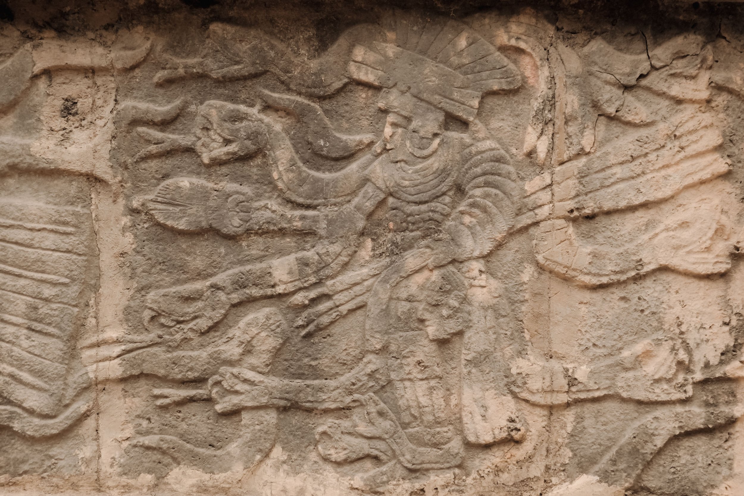 Ancient stone relief of a mythological figure, likely a bird-headed human, carved into a textured stone wall.