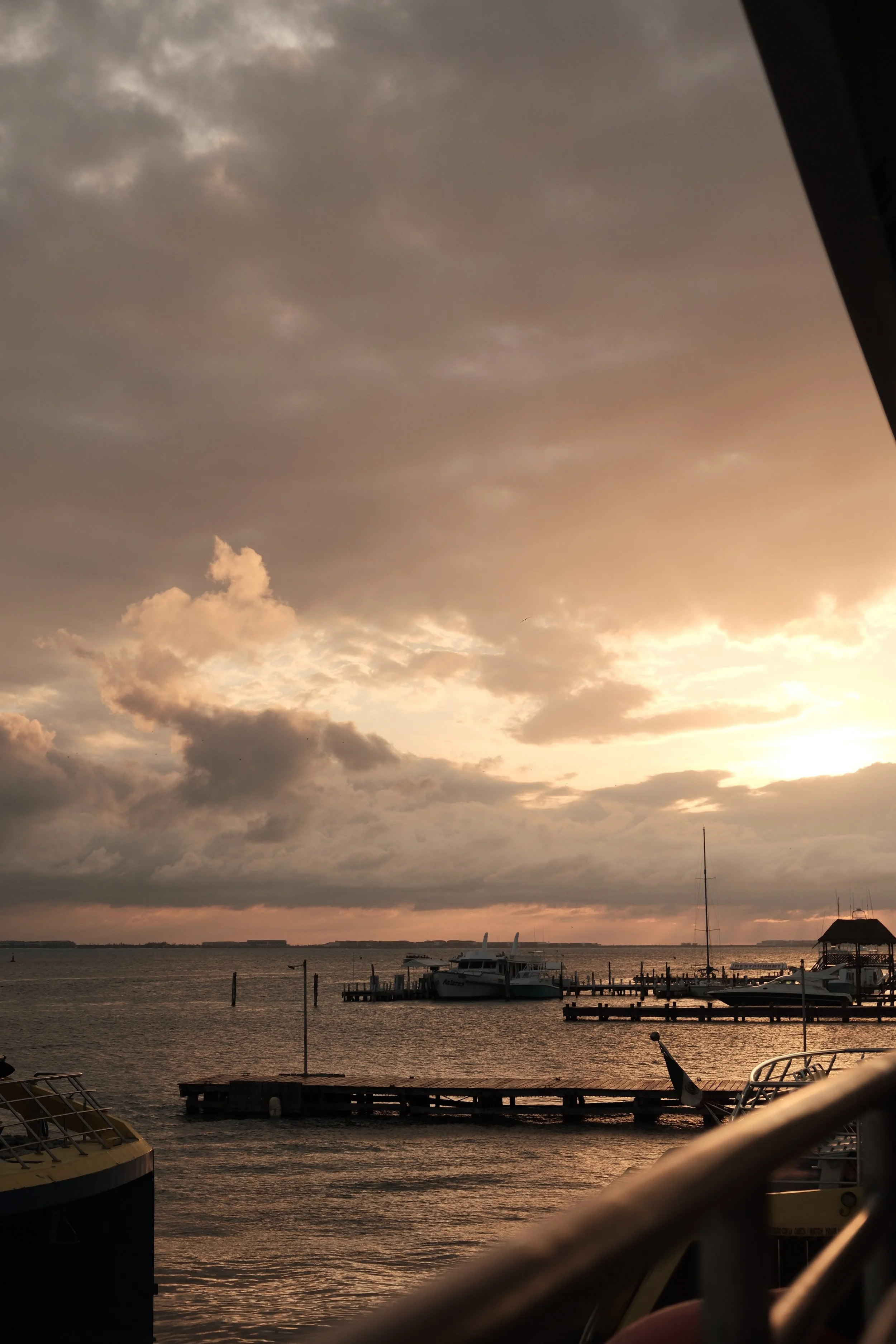 Sunset over a harbor with boats and a dock, cloudy sky, and water reflecting the sunset.