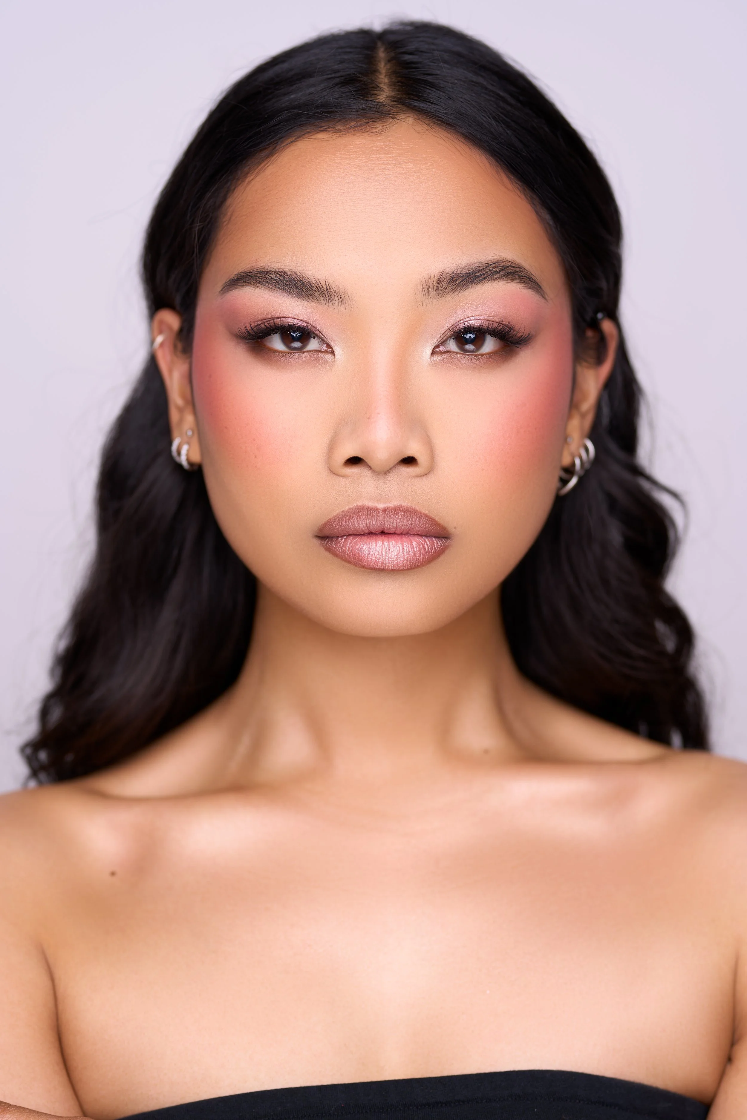 Close-up portrait of a woman with dark wavy hair, makeup, and jewelry, looking directly at the camera.