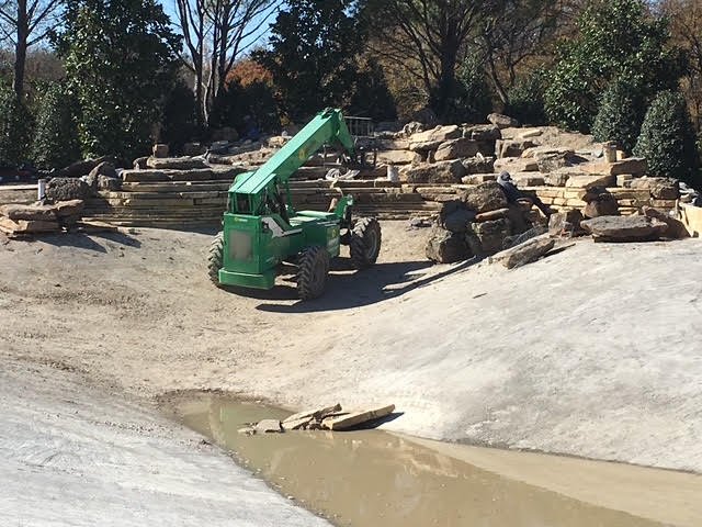 Construction site with a green construction vehicle and rocks stacked in the background.