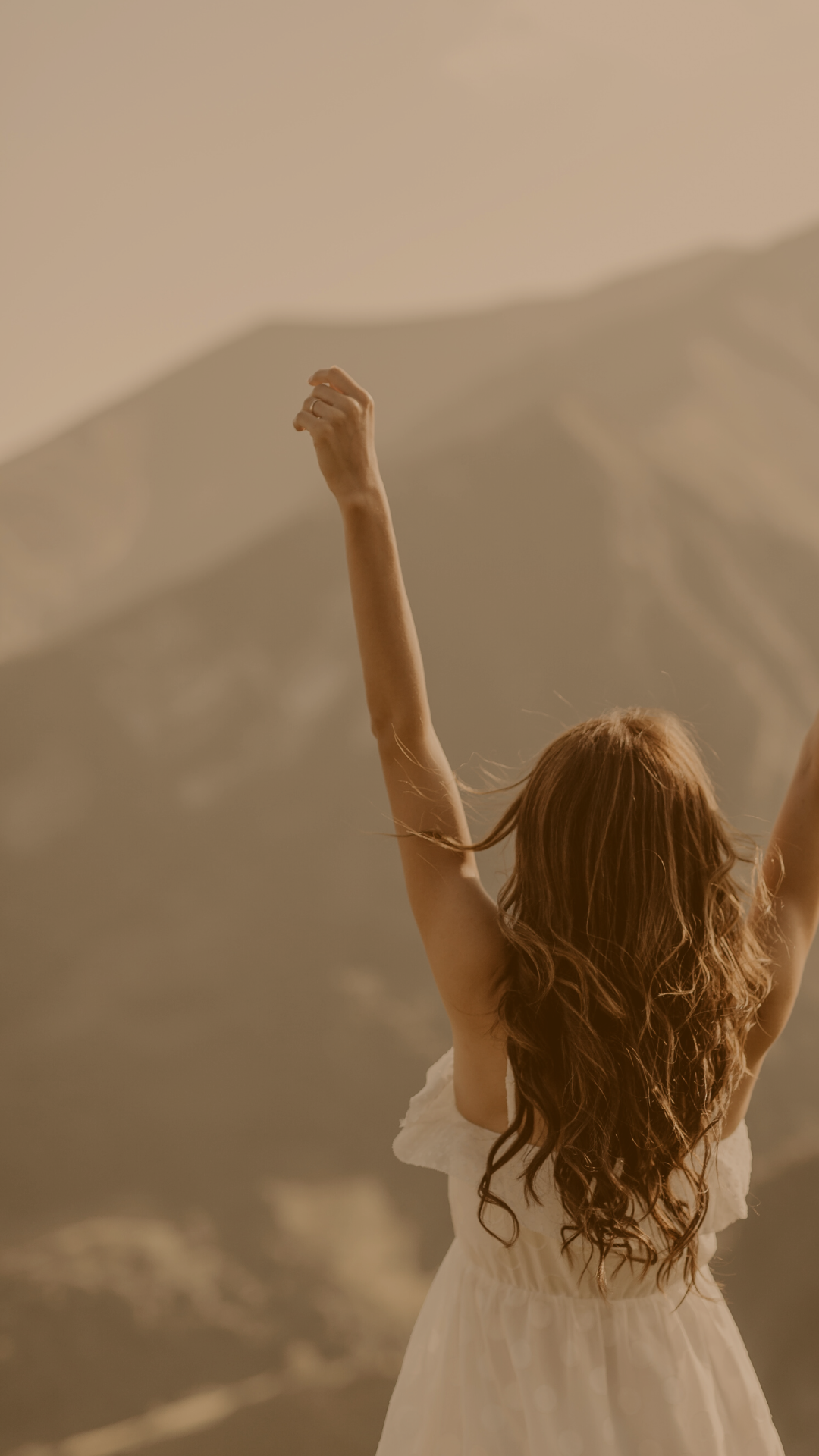 A woman with long red hair raising her arms in front of a mountainous landscape.