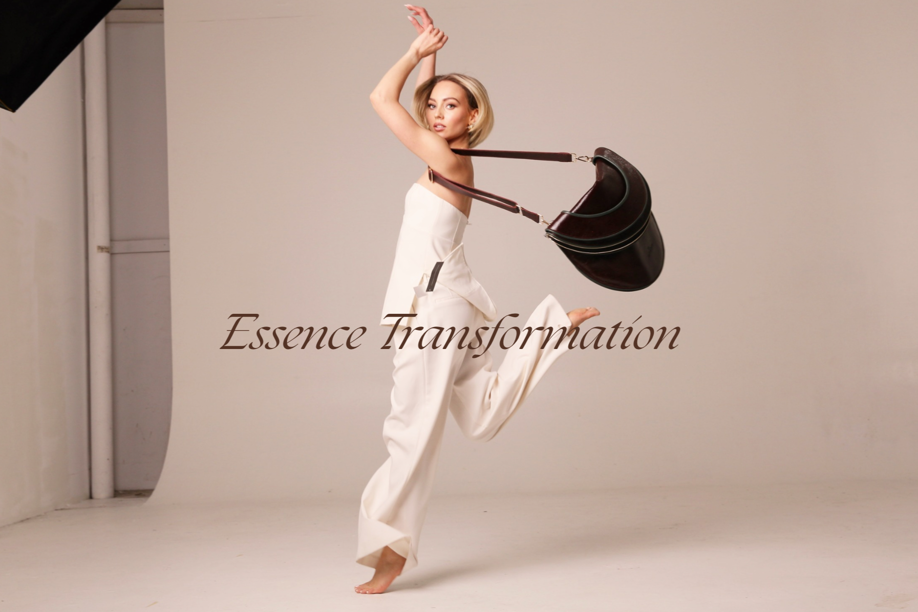 A woman in cream-colored pants and a strapless top poses with one leg raised, holding a black handbag draped around her neck and shoulder, with the phrase 'Essence Transformation' overlaid.