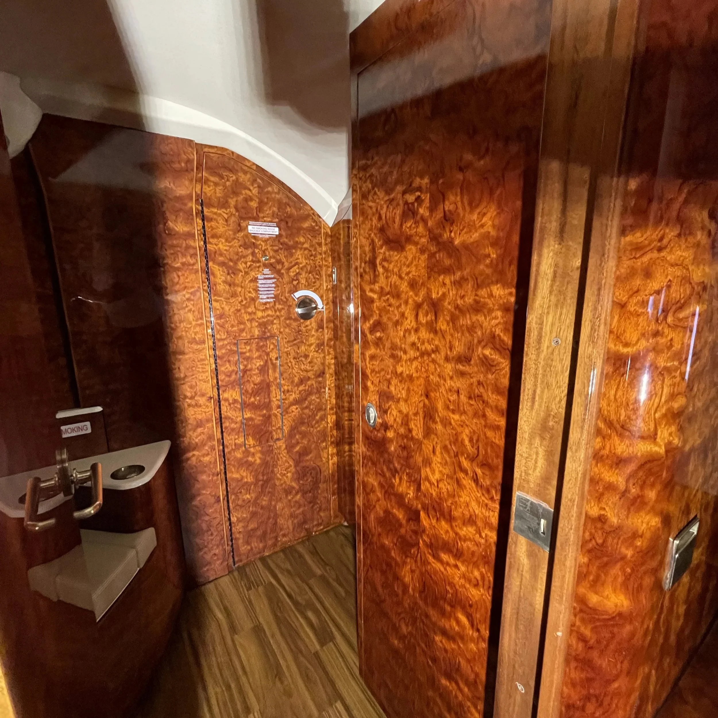 An elevator interior with wood grain paneling, a metal door handle, a mirror, and a small sign on the door. The wood paneling has a shiny, polished finish with intricate grain patterns.