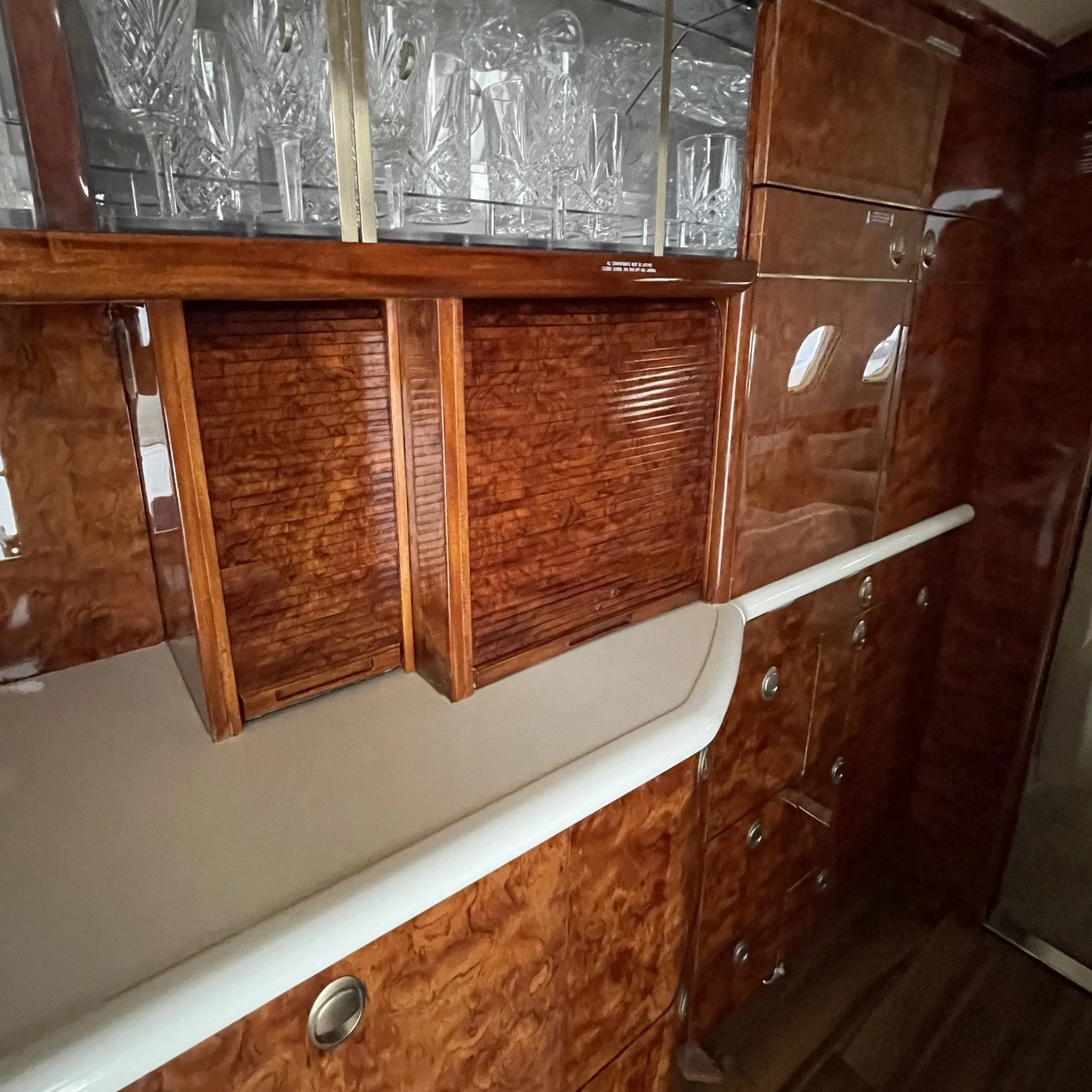 A wooden cabinet with glass doors containing several empty glasses inside, set on a countertop with a wood grain finish.