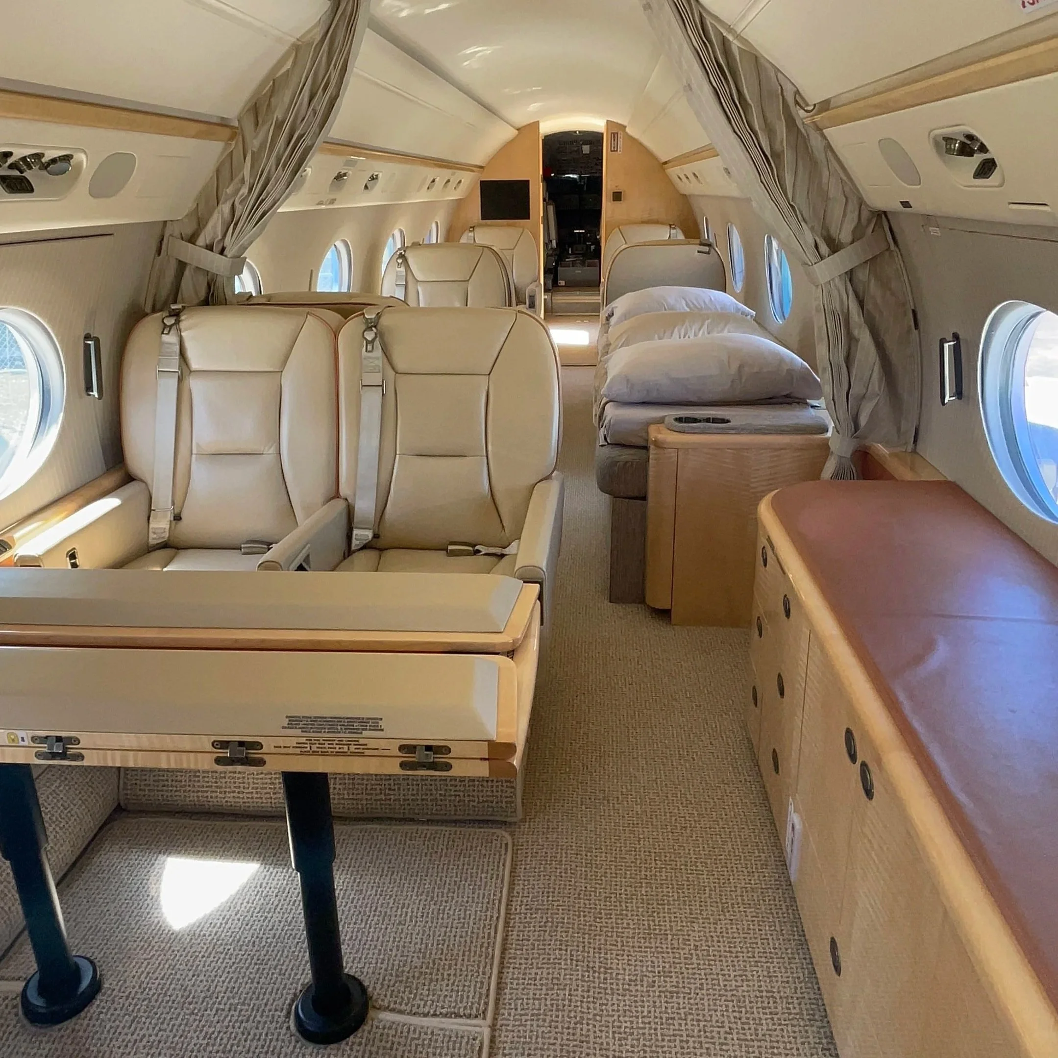 Inside view of an airplane cabin showing beige leather seats, windows, and overhead compartments with closed curtains, part of the cabin floor, and part of the aisle with a black pole.