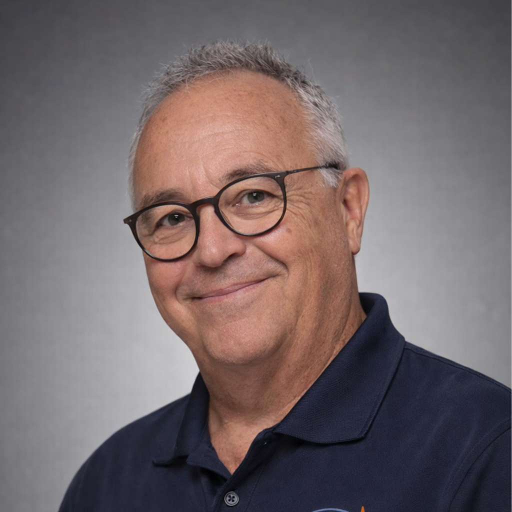 Portrait of a smiling older man with short gray hair and glasses, wearing a navy polo shirt, against a gray background.